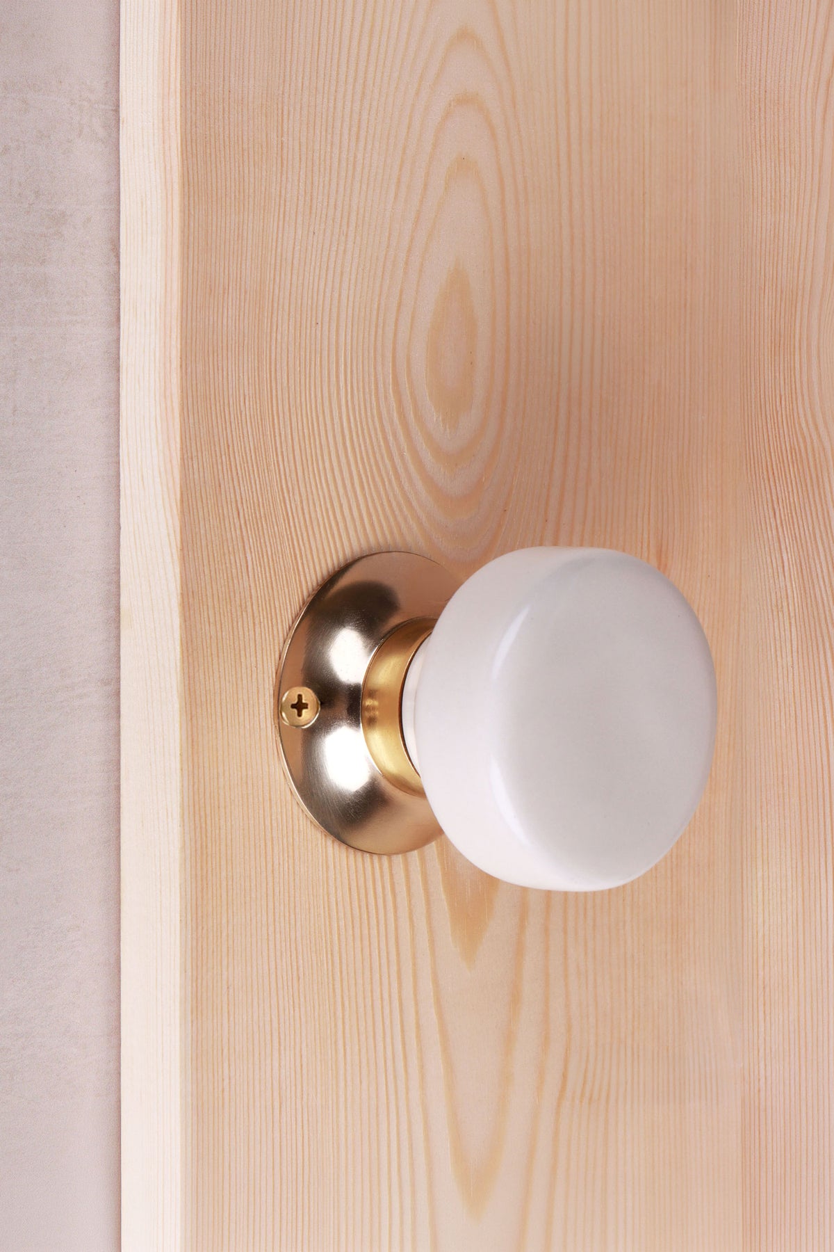 Cream ceramic door knob on a polished brass rose, fitted to a wooden interior door