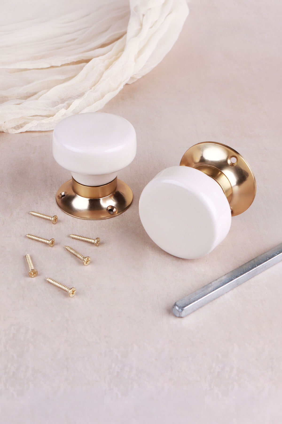 Cream ceramic door knob standing on its polished brass rose beside the second knob, with the spindle and fixing screws