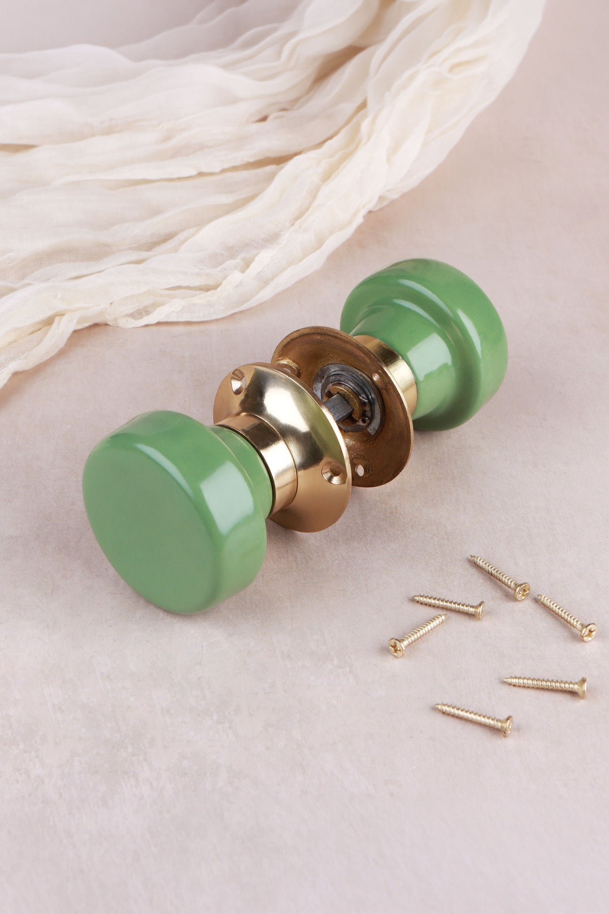 Sage green ceramic mortice door knobs joined by the spindle through their polished brass roses, as they sit on a door
