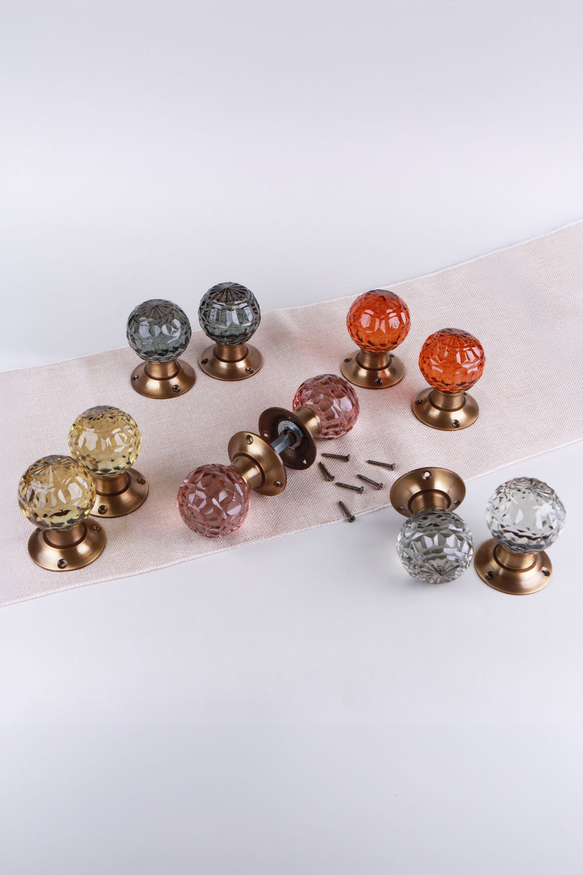 All five colours of the faceted glass mortice door knobs on antique brass roses: smokey grey, amber, blush pink, ivory and clear crystal