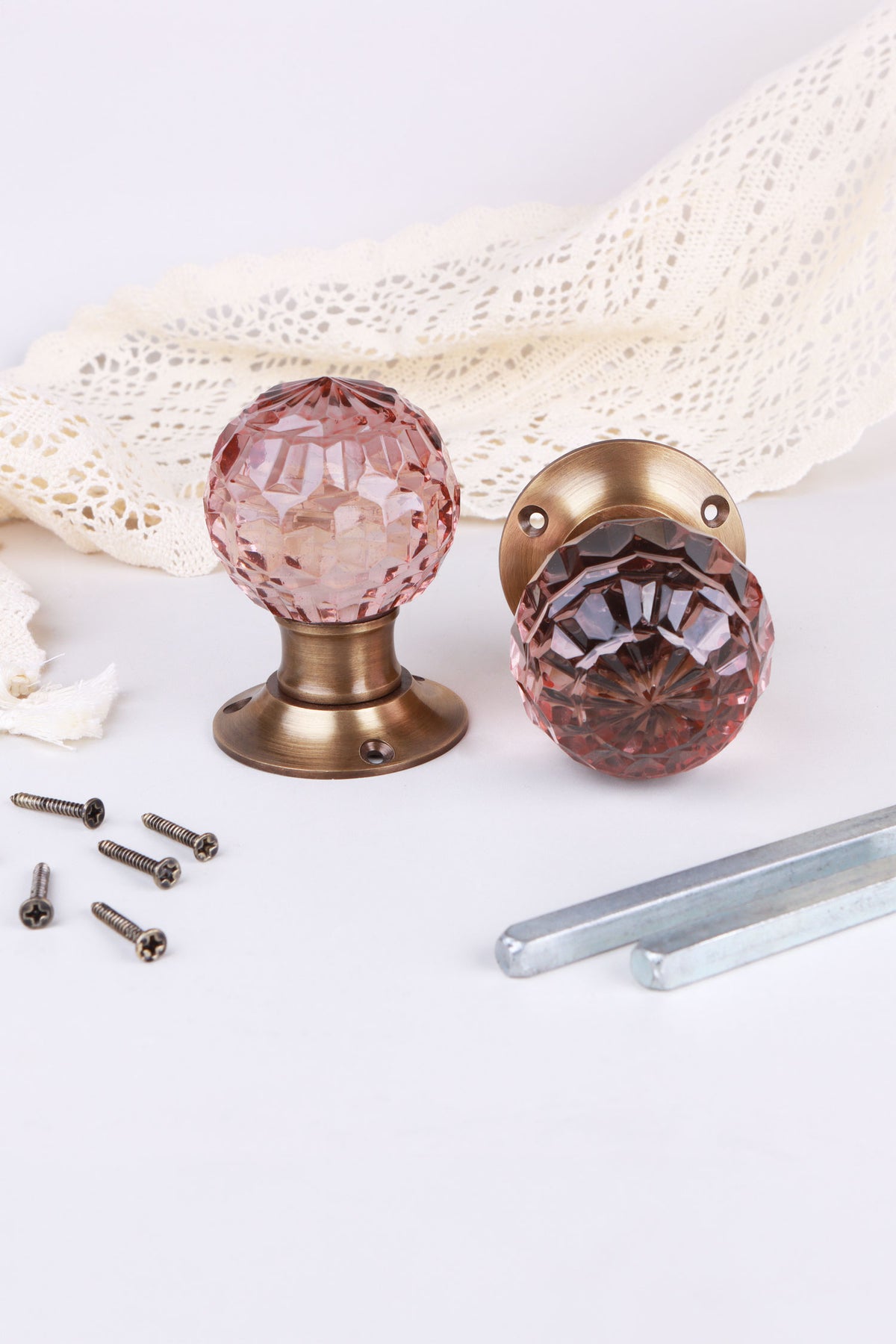 Blush Pink faceted glass door knob standing on its antique brass rose beside the second knob lying on its side, with the spindles and screws