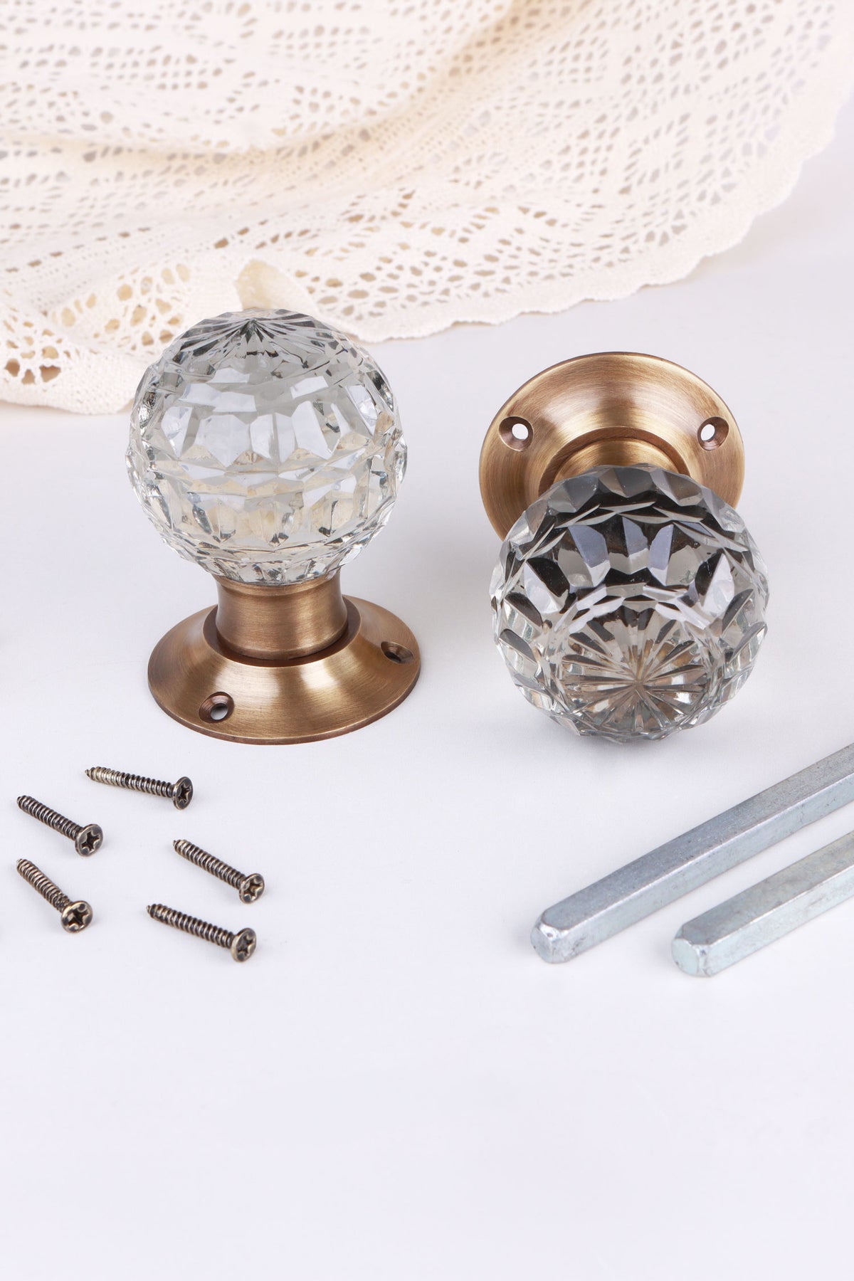 Clear Crystal faceted glass door knob standing on its antique brass rose beside the second knob lying on its side, with the spindles and screws