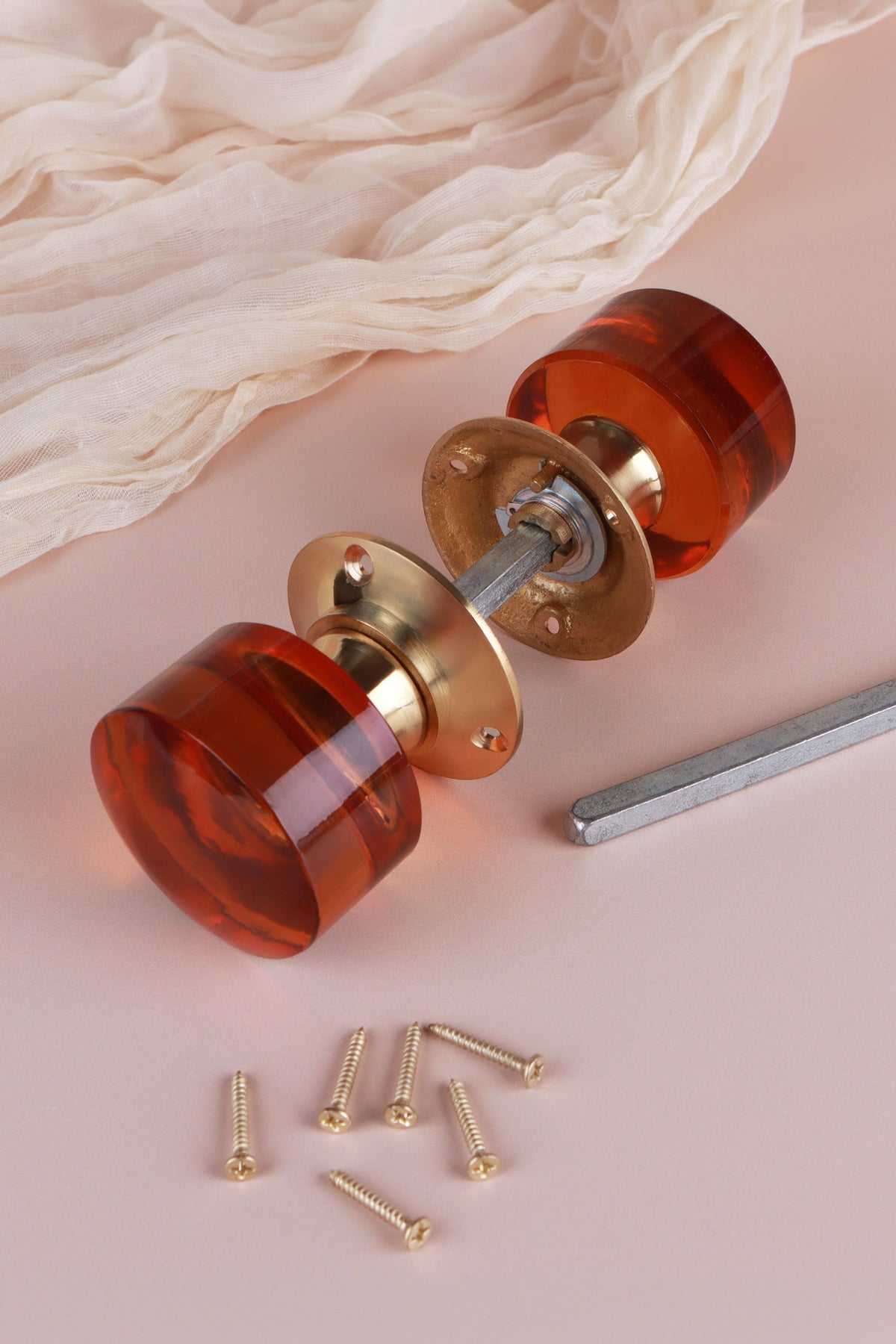 Amber glass cylinder mortice door knobs joined by the spindle through their polished brass roses, as they sit on a door