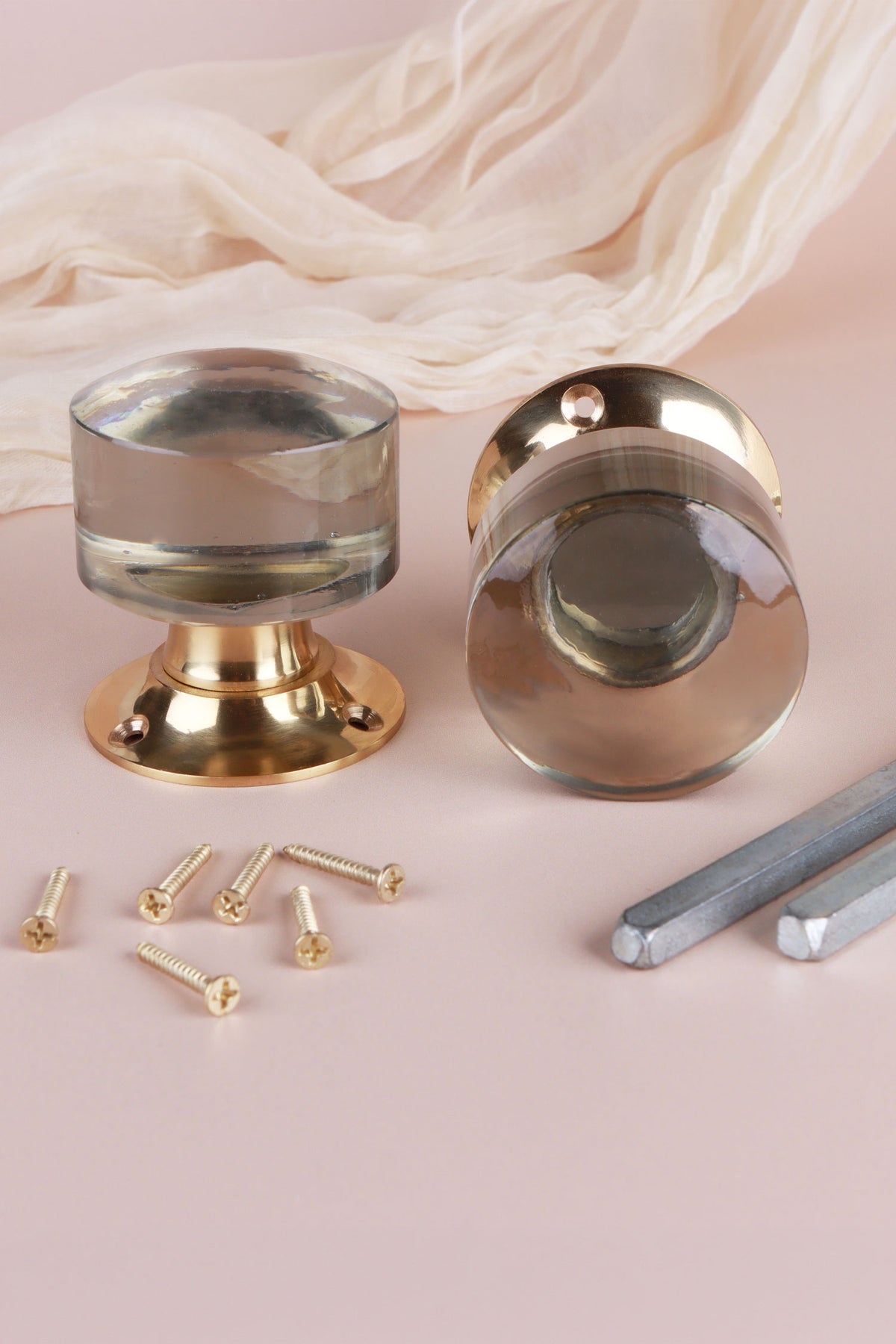 Pair of clear glass cylinder mortice door knobs on polished brass roses, one standing and one on its side, with the square spindles and fixing screws
