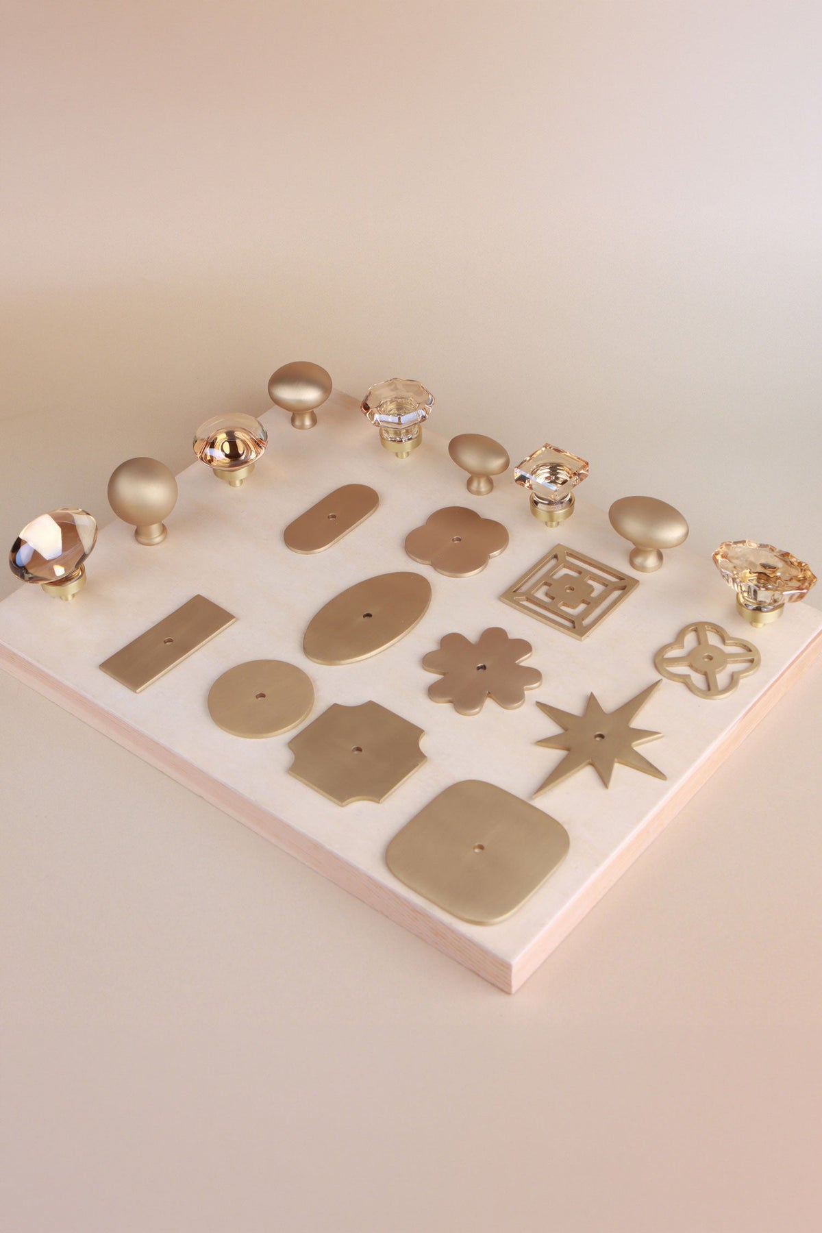 Eleven satin brass backplate shapes laid out on a board with champagne crystal and satin brass knobs