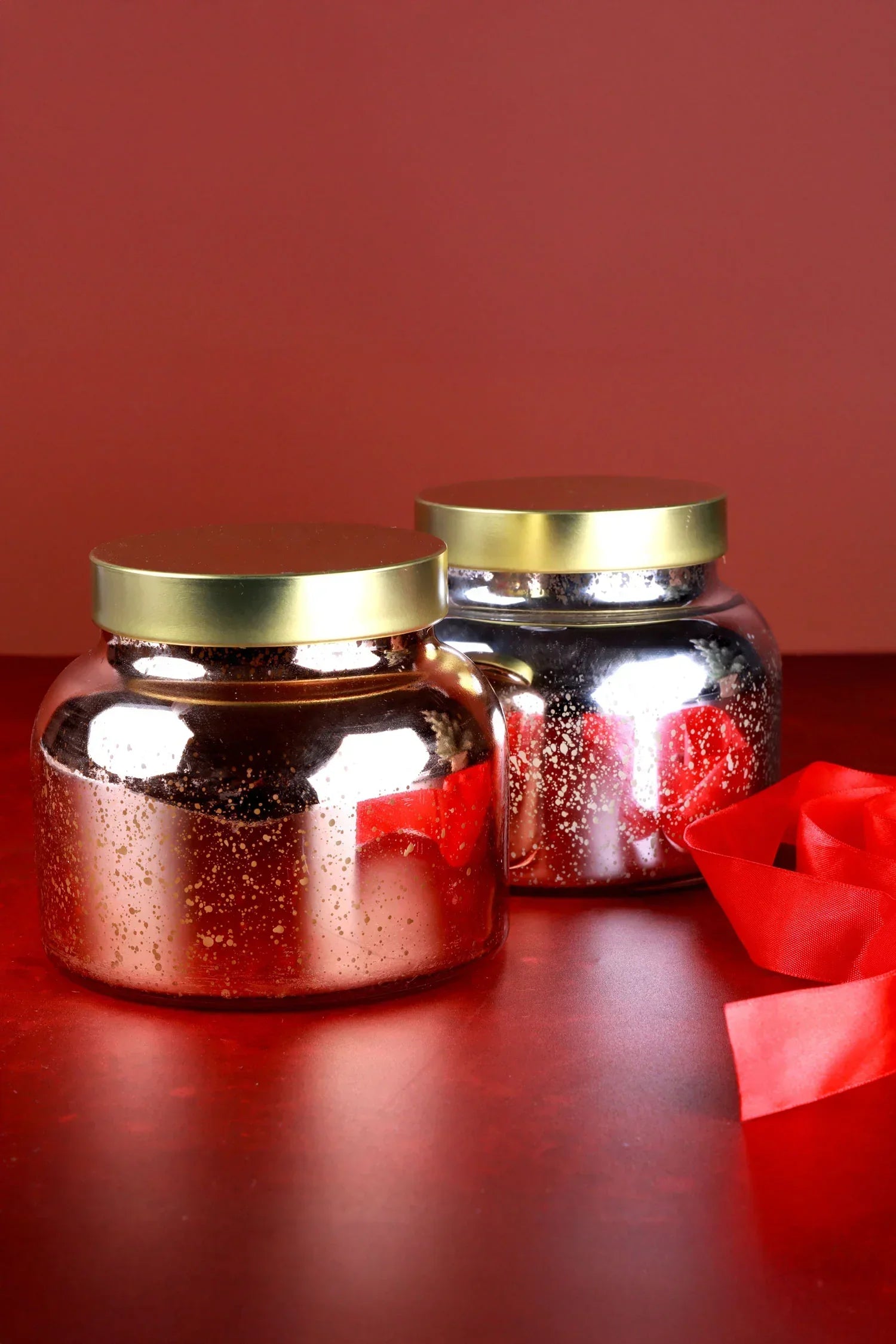 Metallic gold and silver G Decor candles in glass jars with gold lids, on a red surface