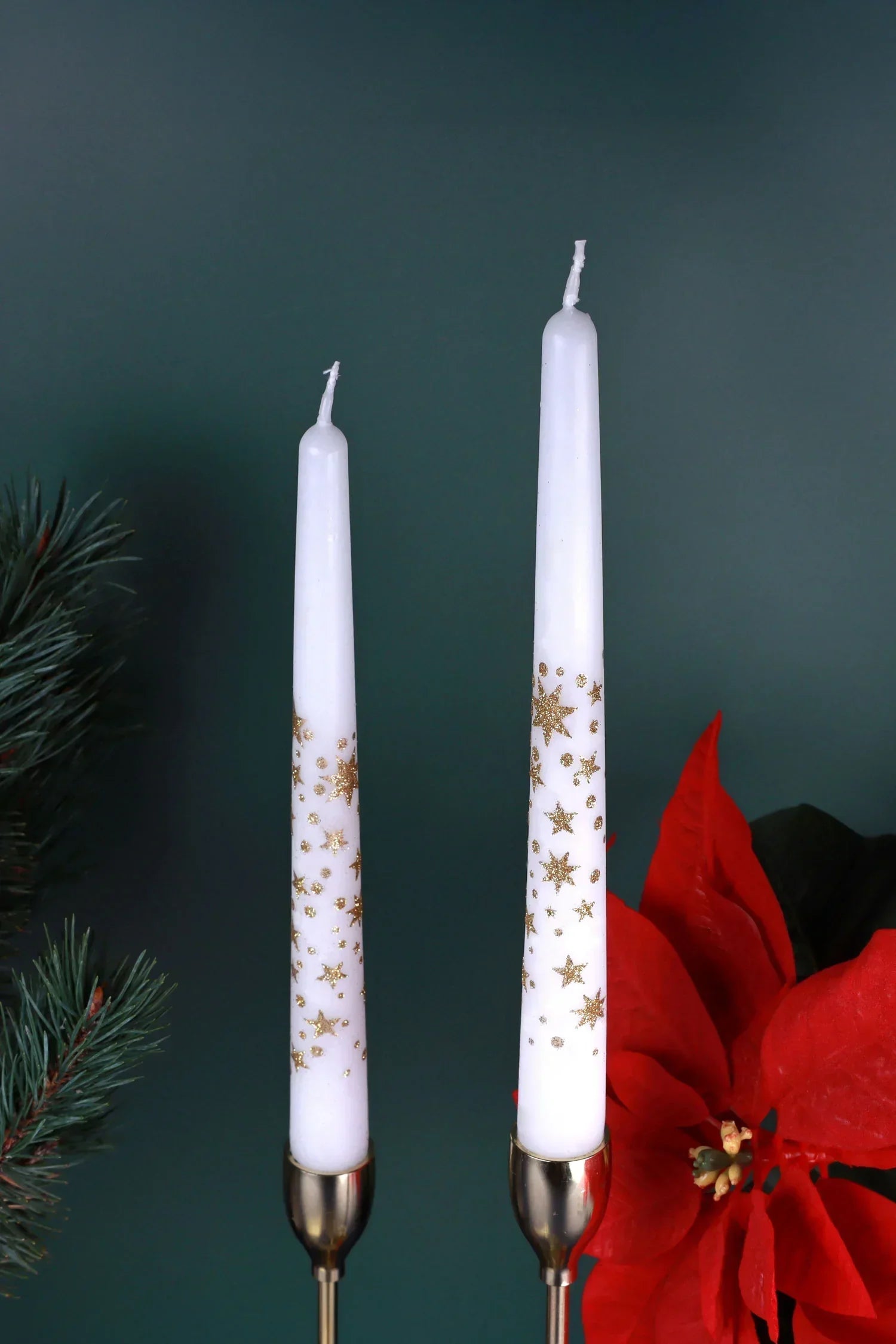 White taper candles with gold star designs in holders, festive decor with poinsettia, G Decor