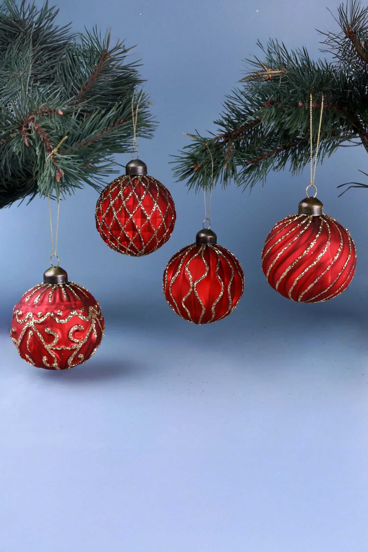 Red glass Christmas baubles with gold detailing hanging on pine branches, G Decor holiday décor