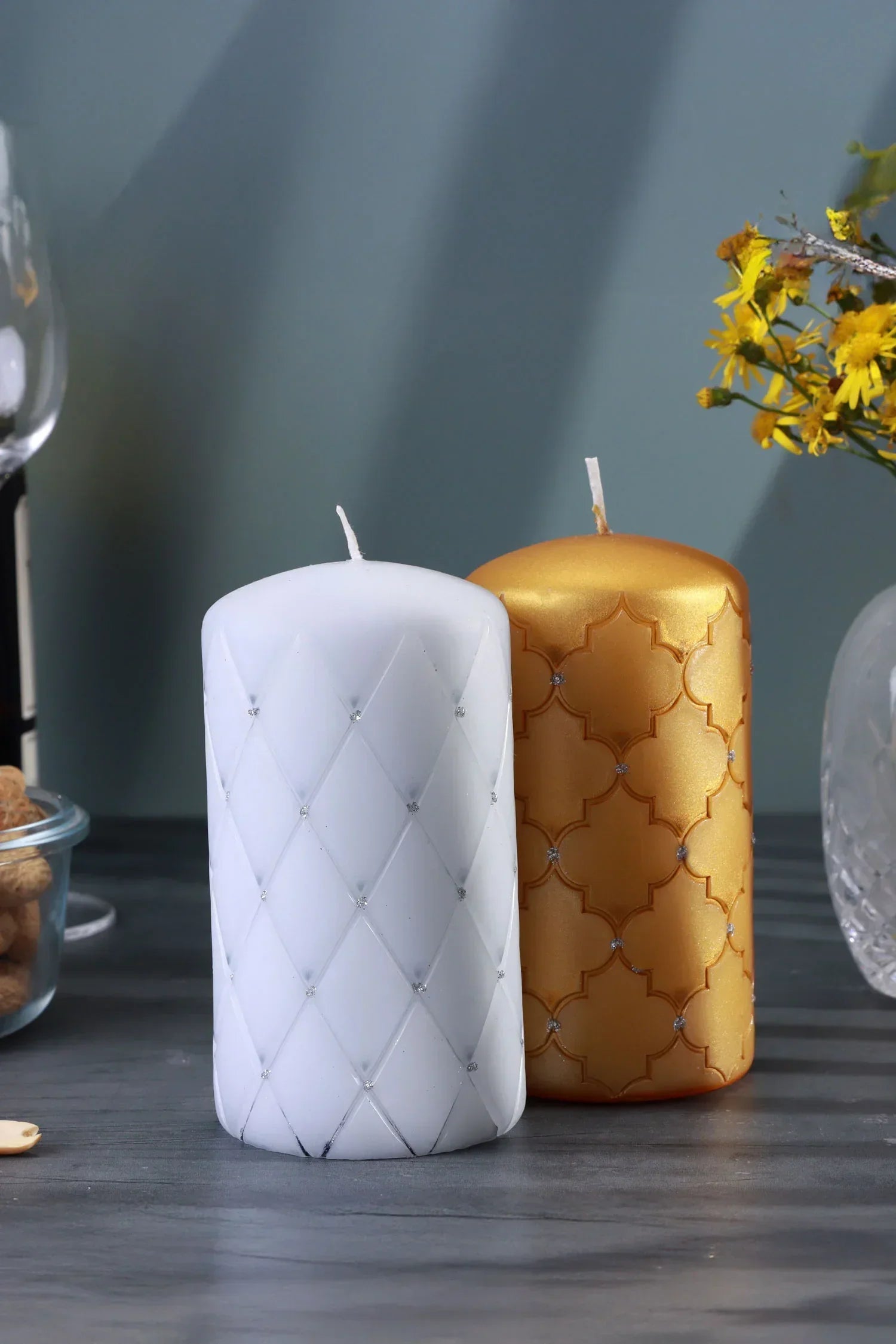 Luxury white and gold decorative pillar candles on a table with flowers and glassware