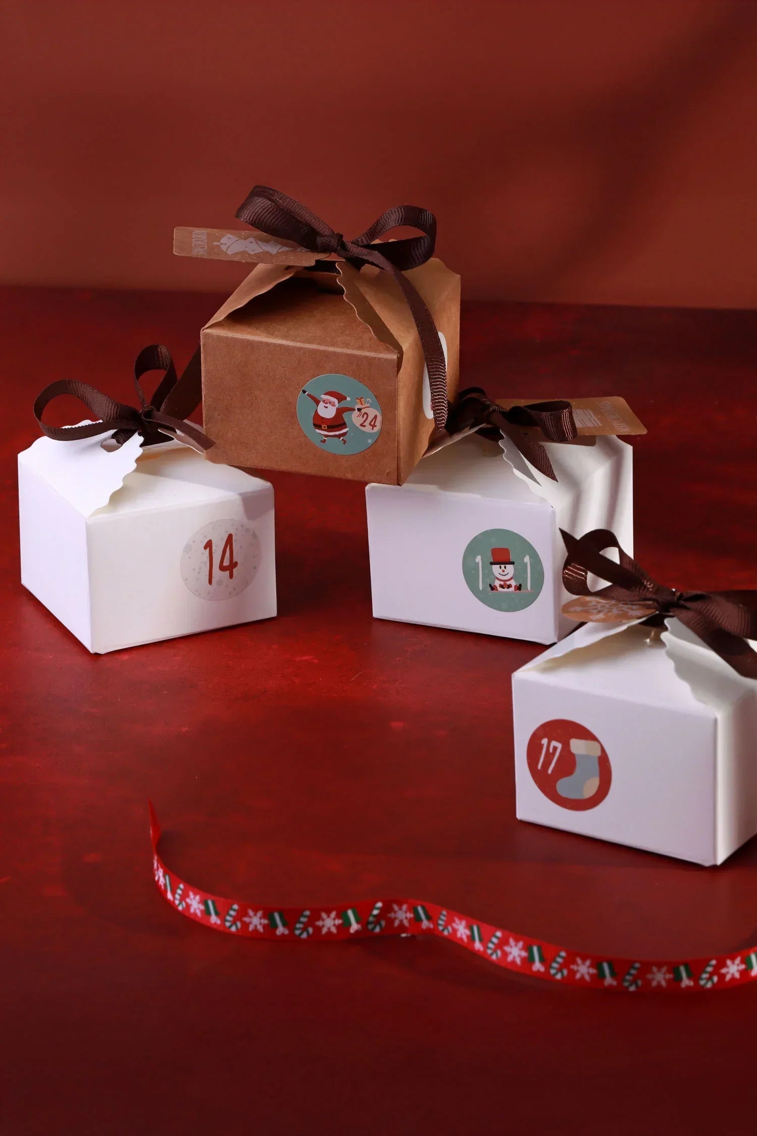 Festive gift boxes with brown ribbons and holiday stickers, styled on a red background from G Decor.