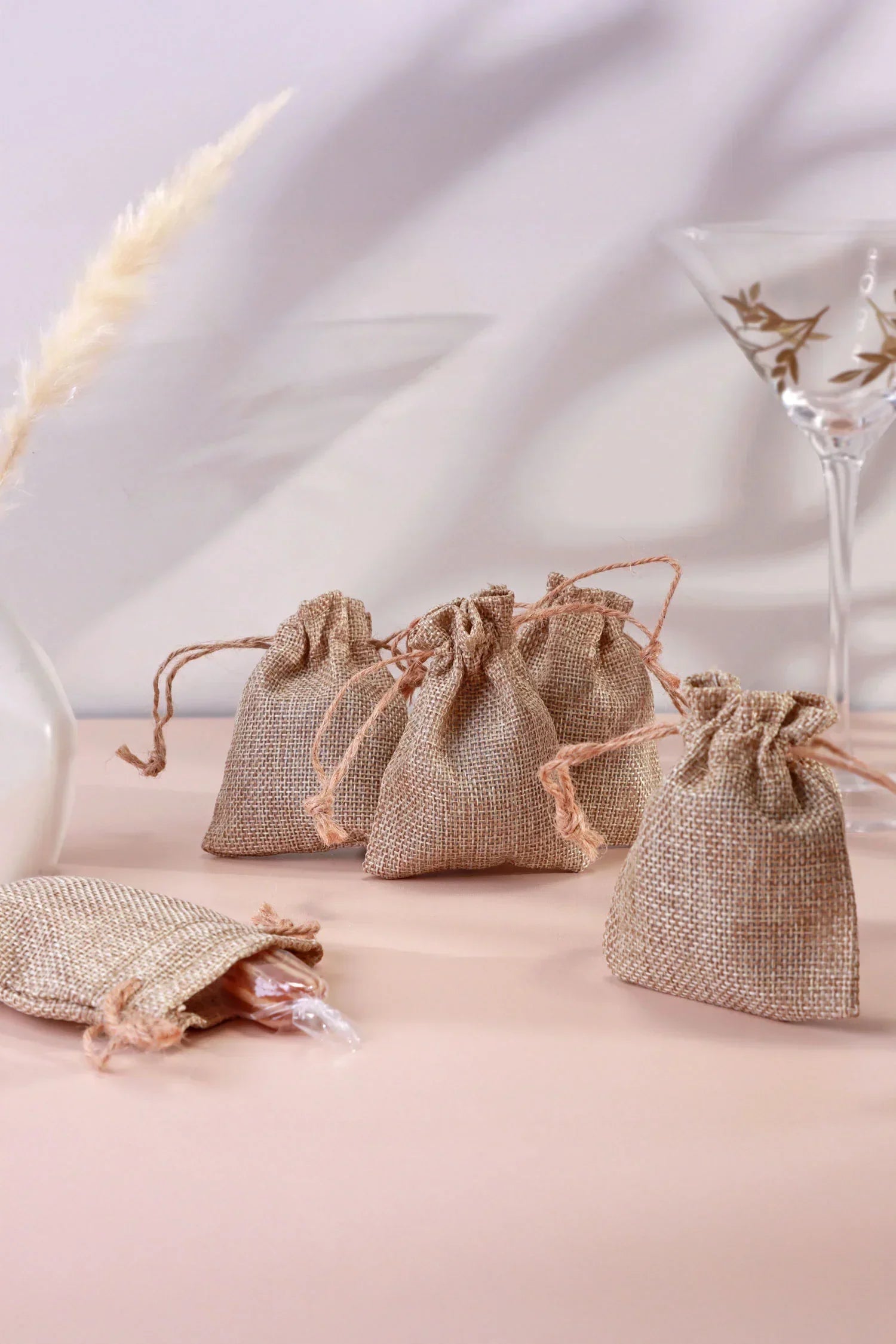 Set of small burlap gift pouches with gold decor and glassware on a pastel surface, G Decor.