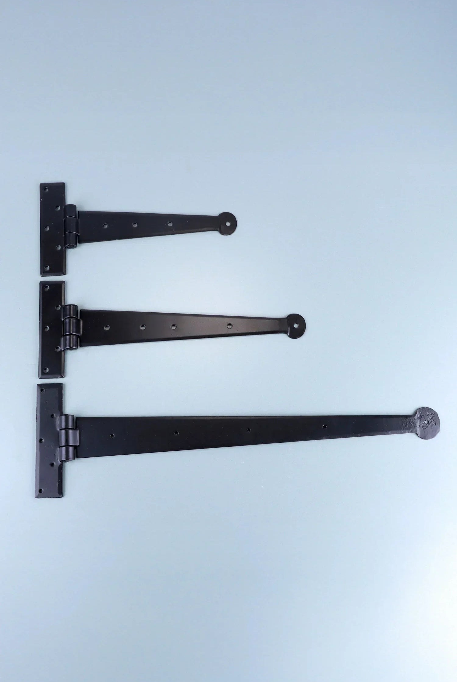 Three black T-hinges of varying sizes displayed on a light background, G Decor hardware