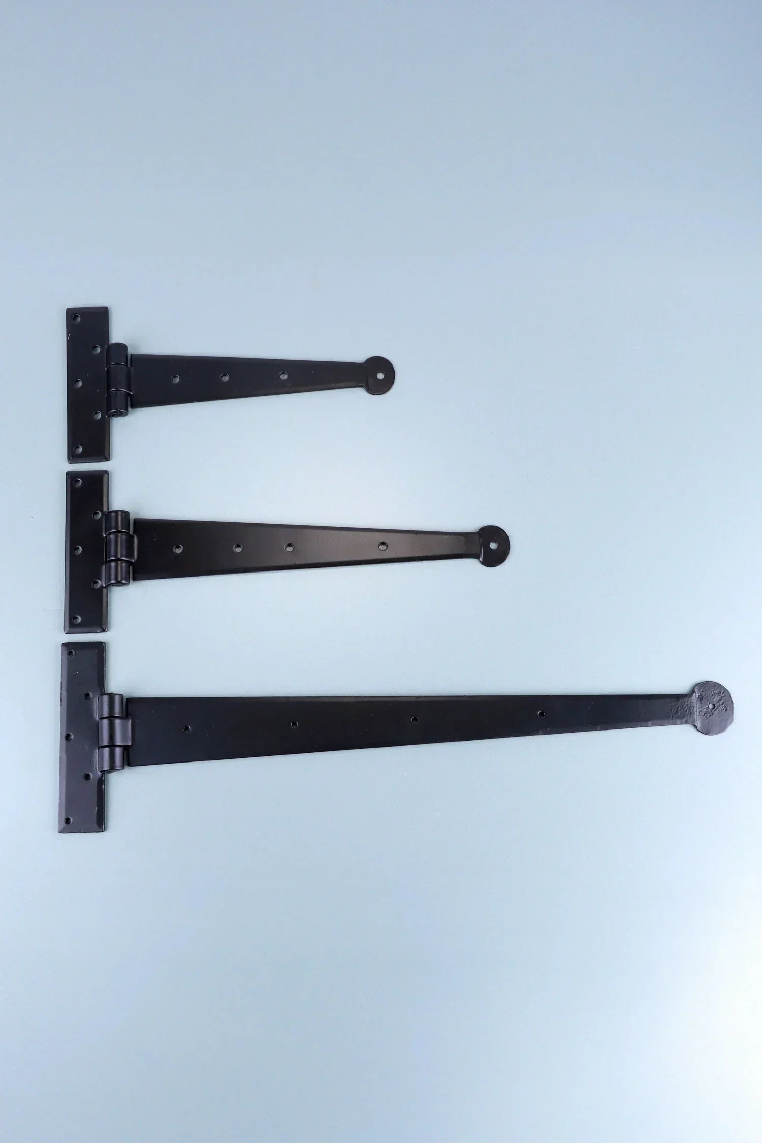 Three black T-hinges of varying sizes displayed on a light background, G Decor hardware