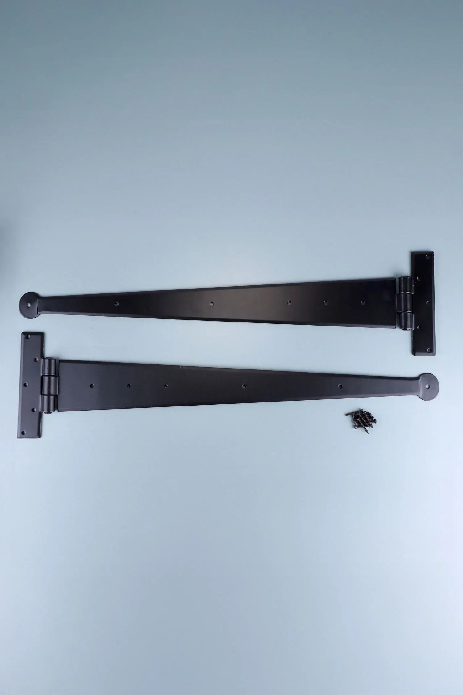 Pair of black metal T-hinges with screws on a light surface, G Decor luxury hardware