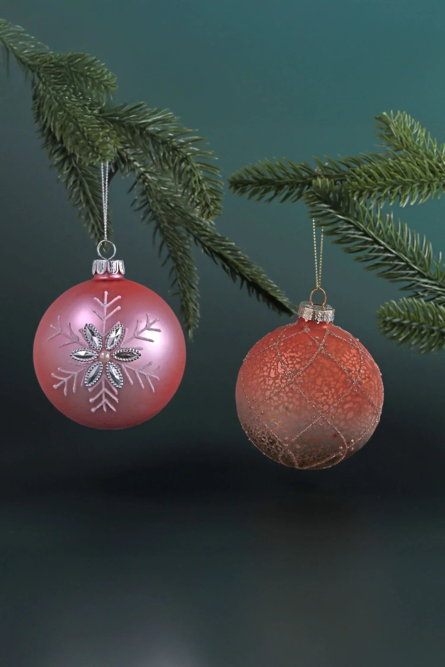 Luxury pink Christmas baubles with intricate designs hanging from pine branches