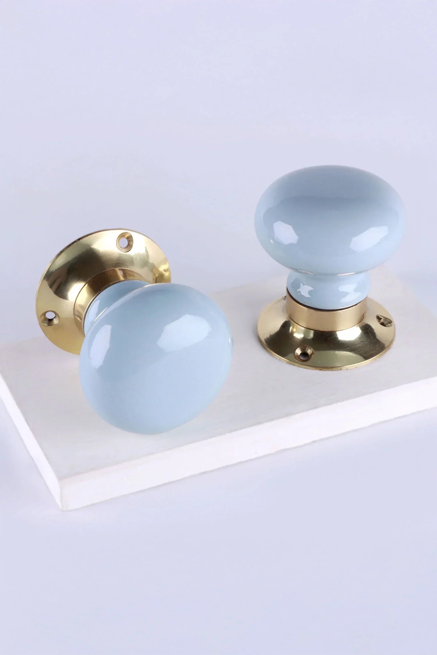Pair of G Decor light blue ceramic and gold door knobs on white background, luxury hardware