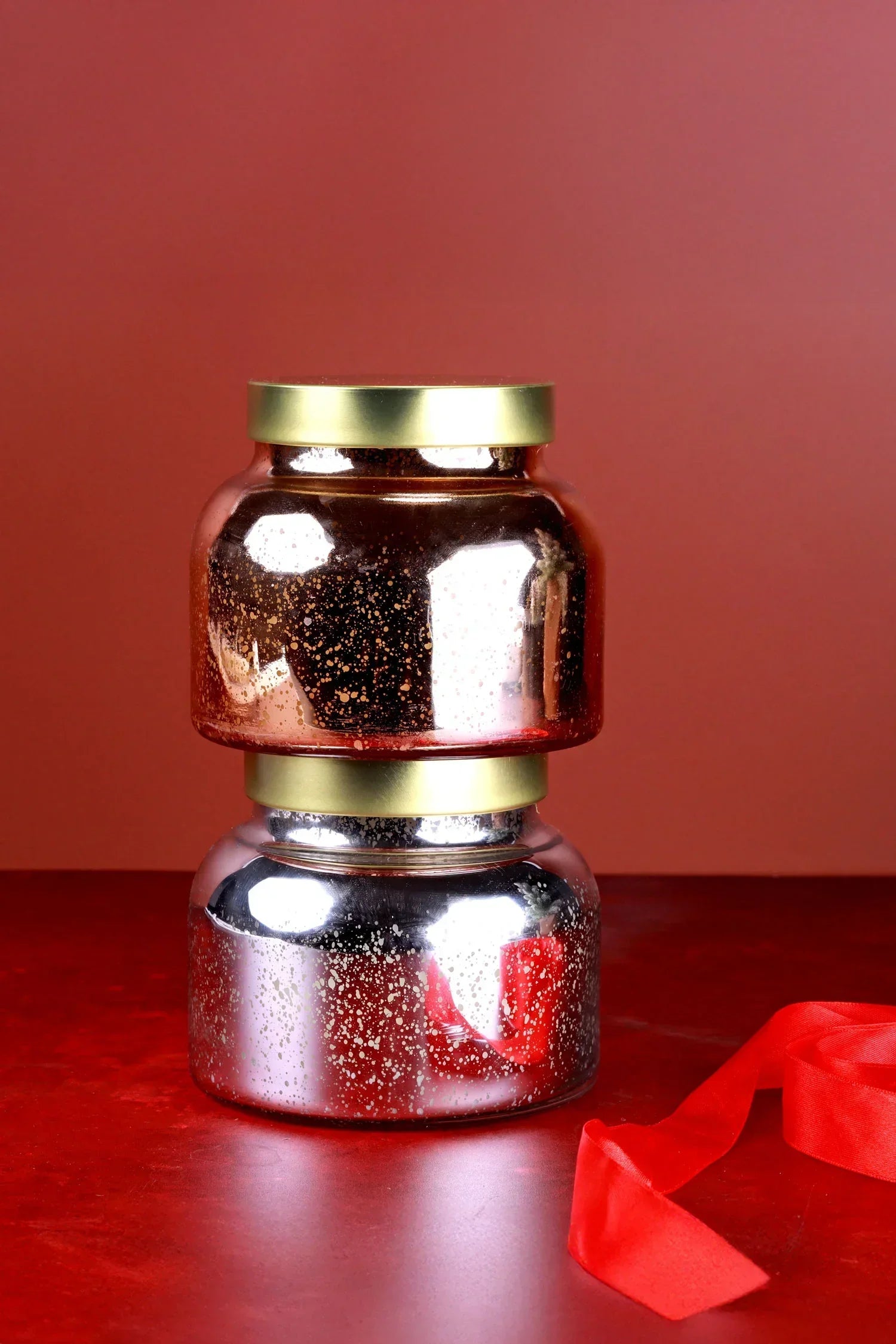 Two metallic glass jars with gold lids stacked on a red surface, luxury home decor by G Decor