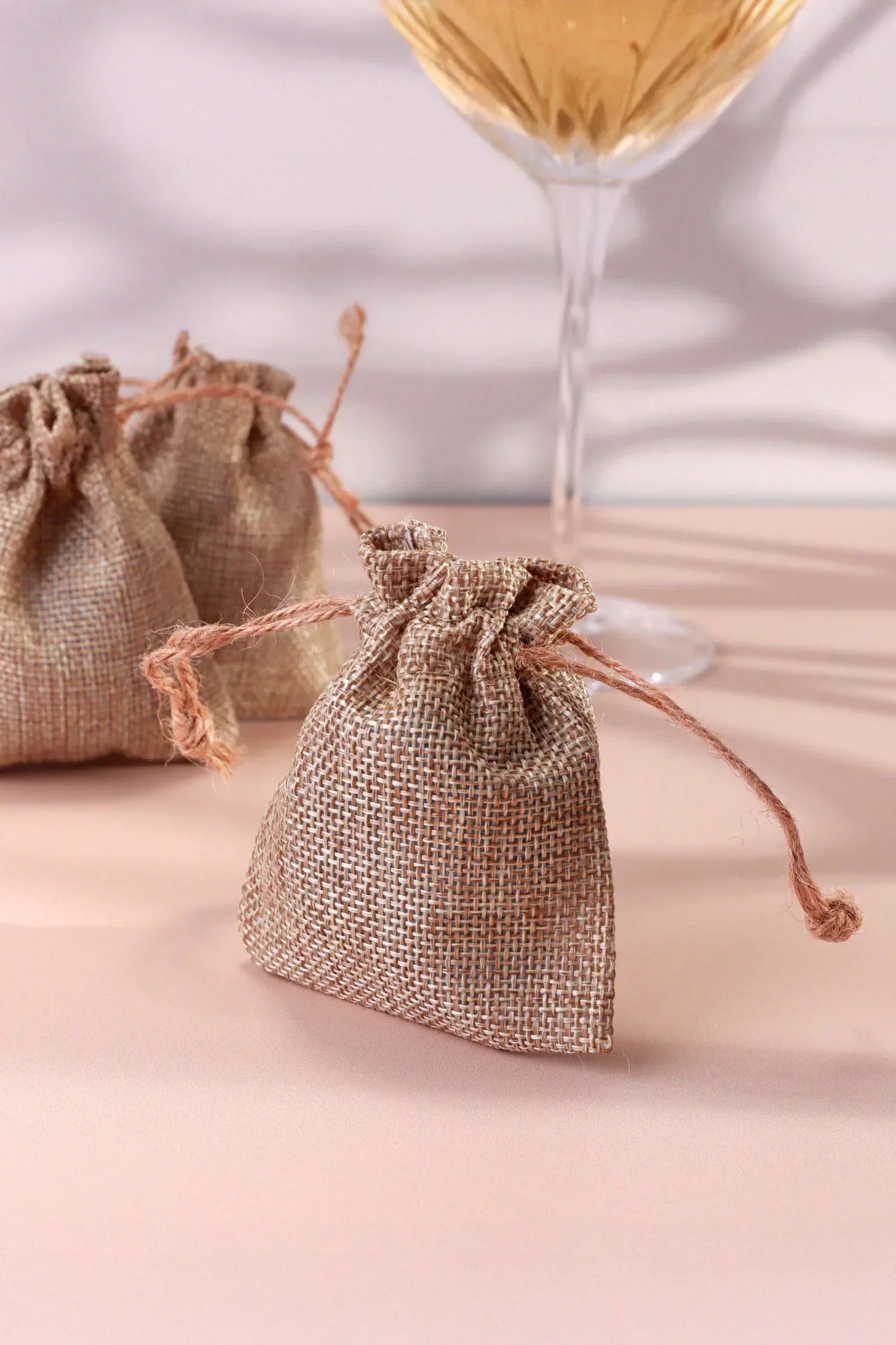 Decorative burlap drawstring bags with glassware on a pastel tabletop, luxury home décor