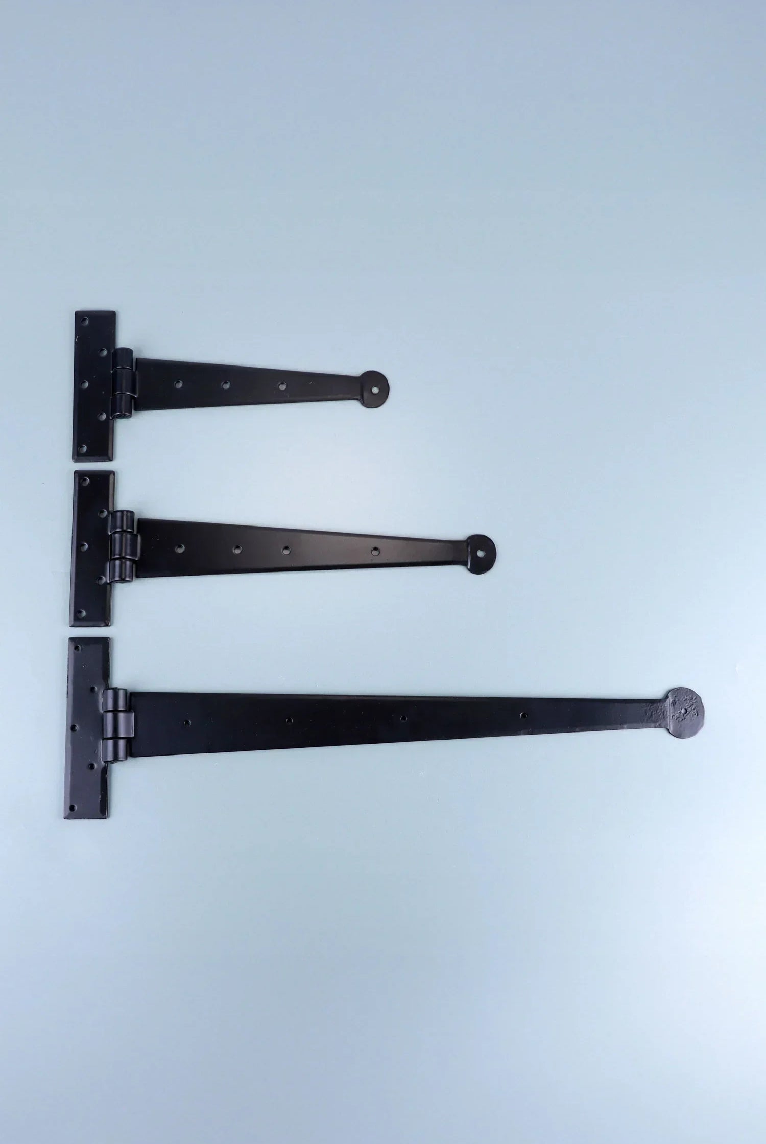Three black decorative T hinges in different sizes on a light blue background, G Decor hardware