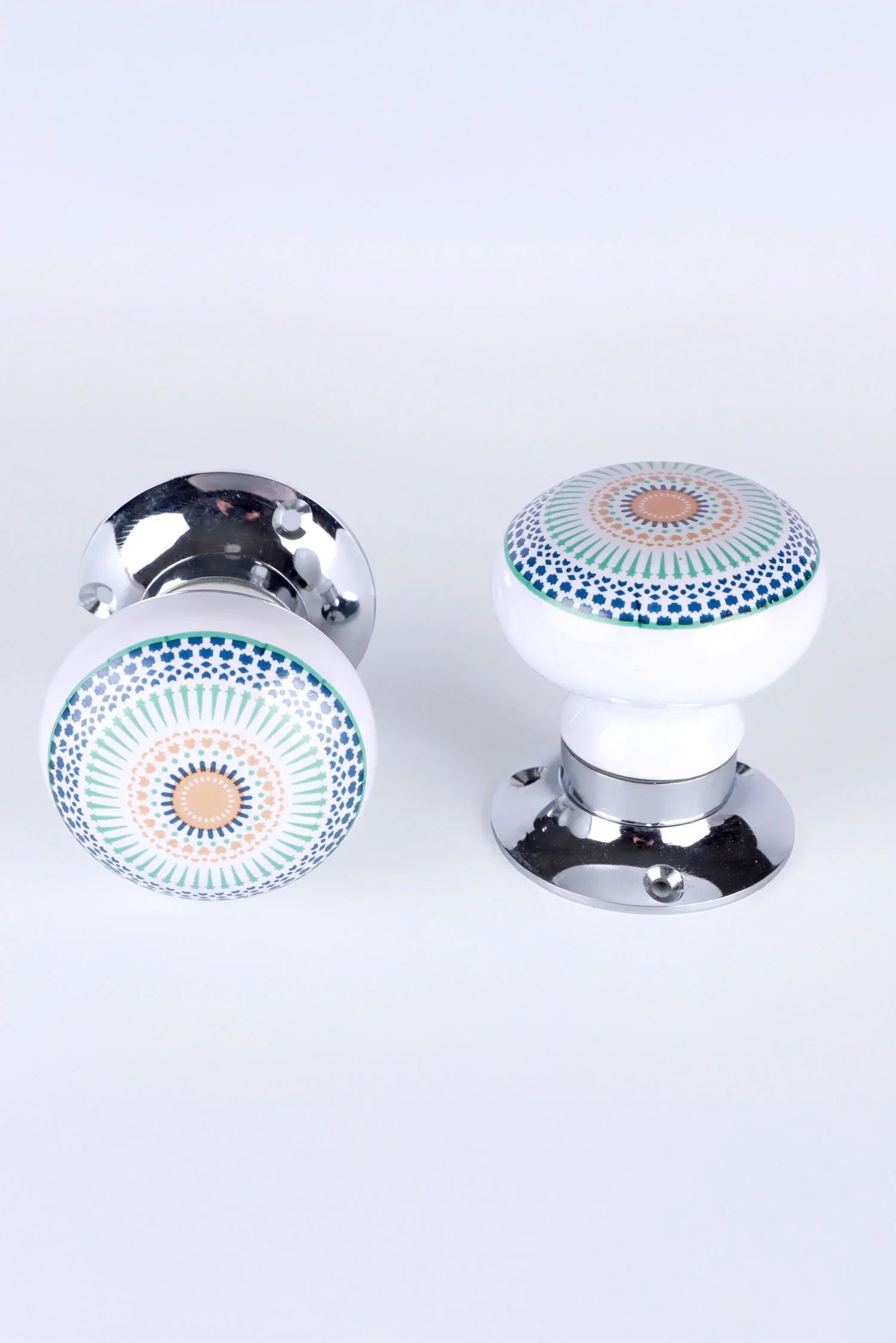Pair of G Decor ceramic and chrome door knobs with intricate geometric patterns on white background