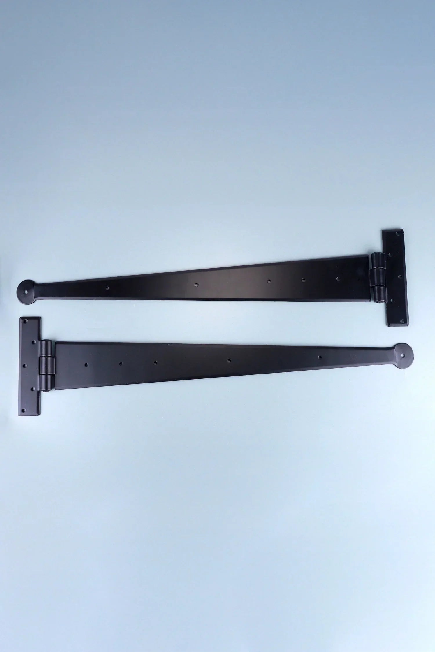 Pair of black metal strap hinges on light blue background, luxury hardware by G Decor