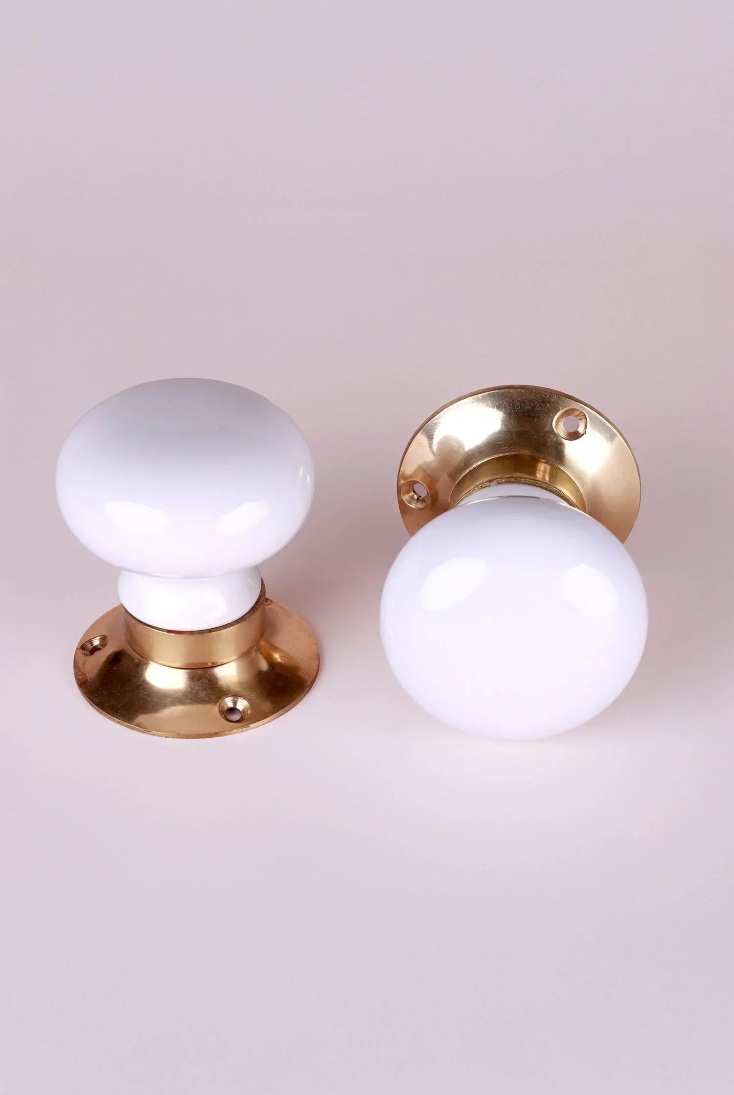 Pair of G Decor white ceramic and gold door knobs on a light background