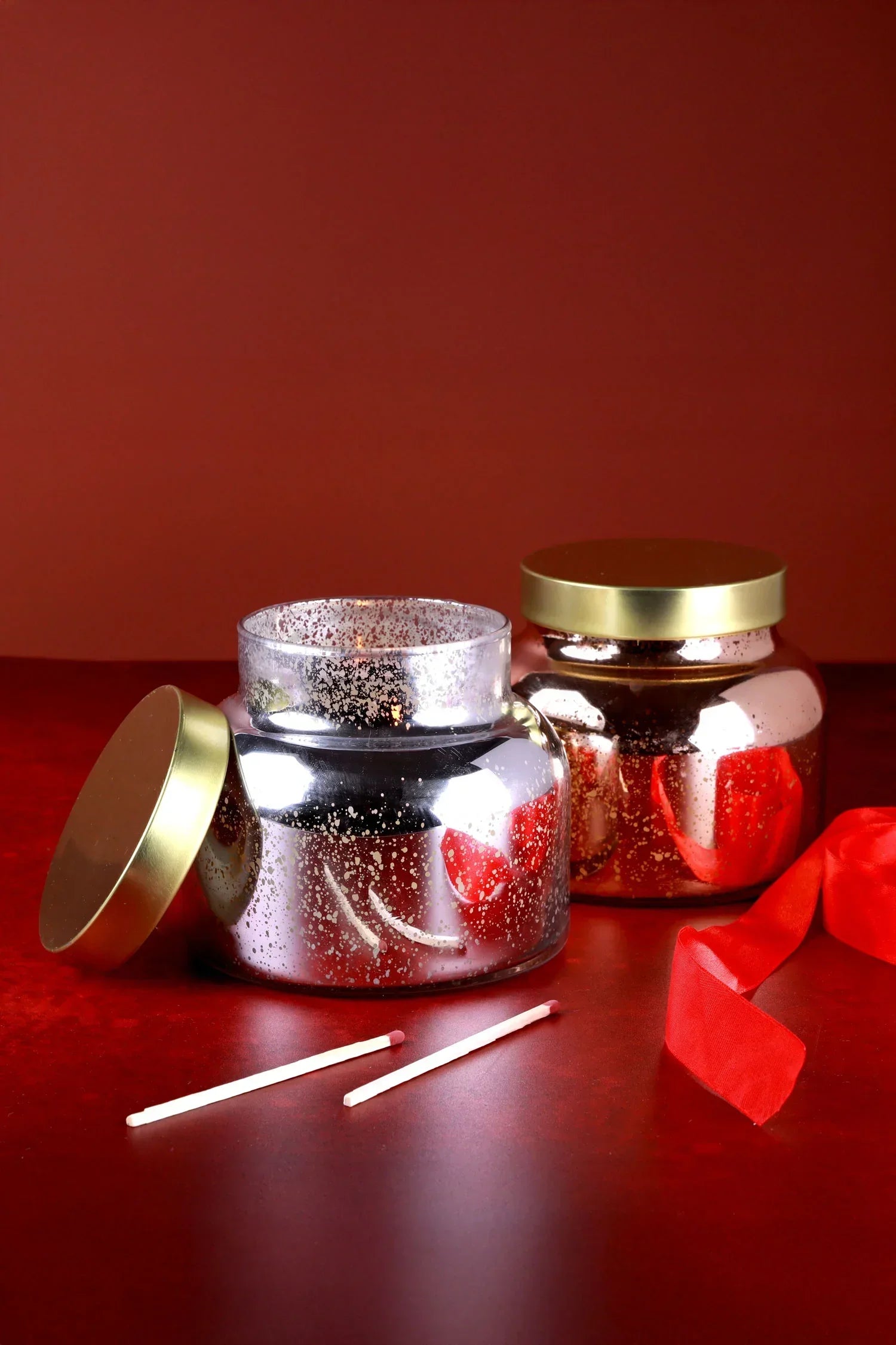 Luxury G Decor metallic candle jars with gold lids, red ribbon, and matches on red background