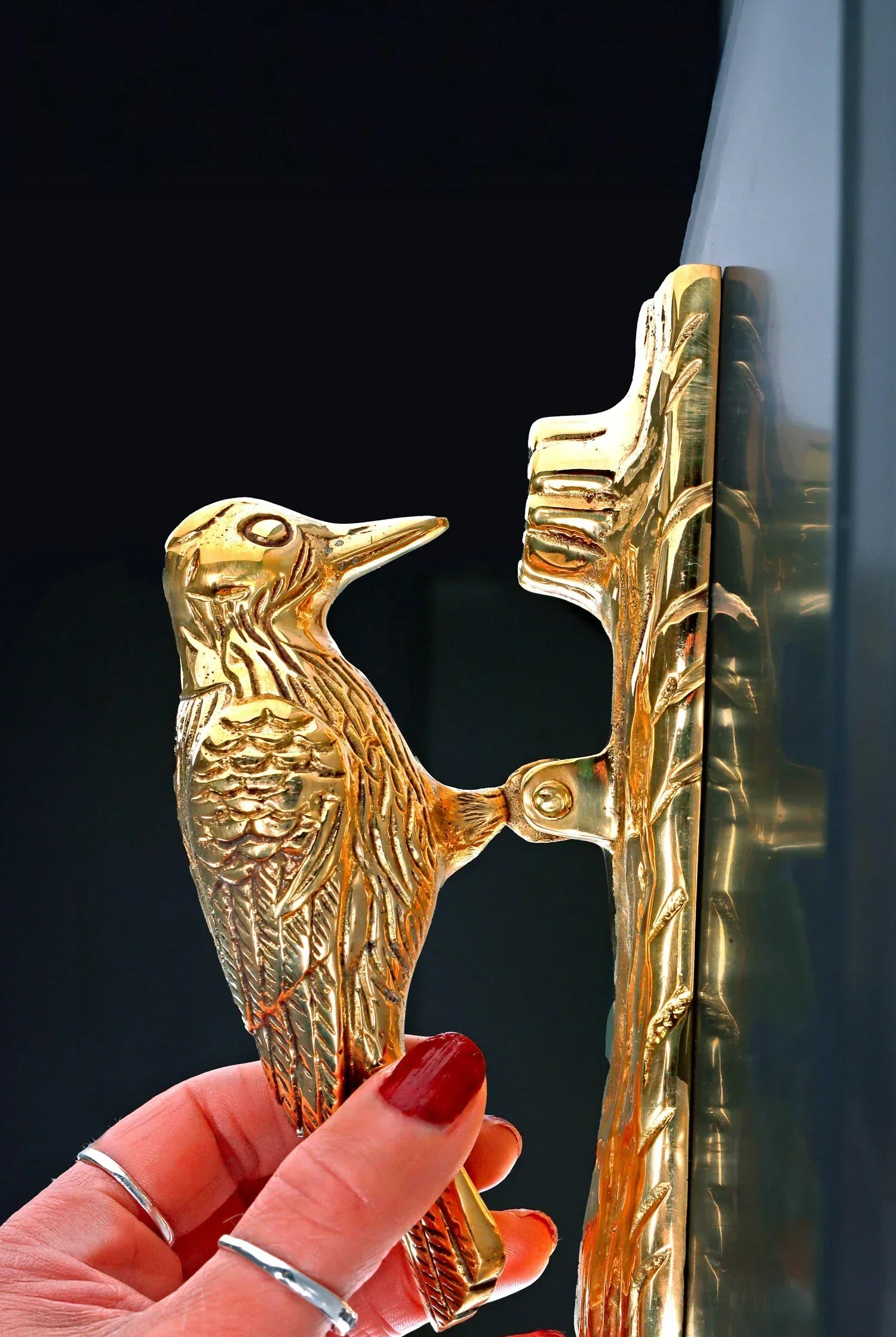 Gold woodpecker door knocker by G Decor, luxury home hardware, held against a dark door