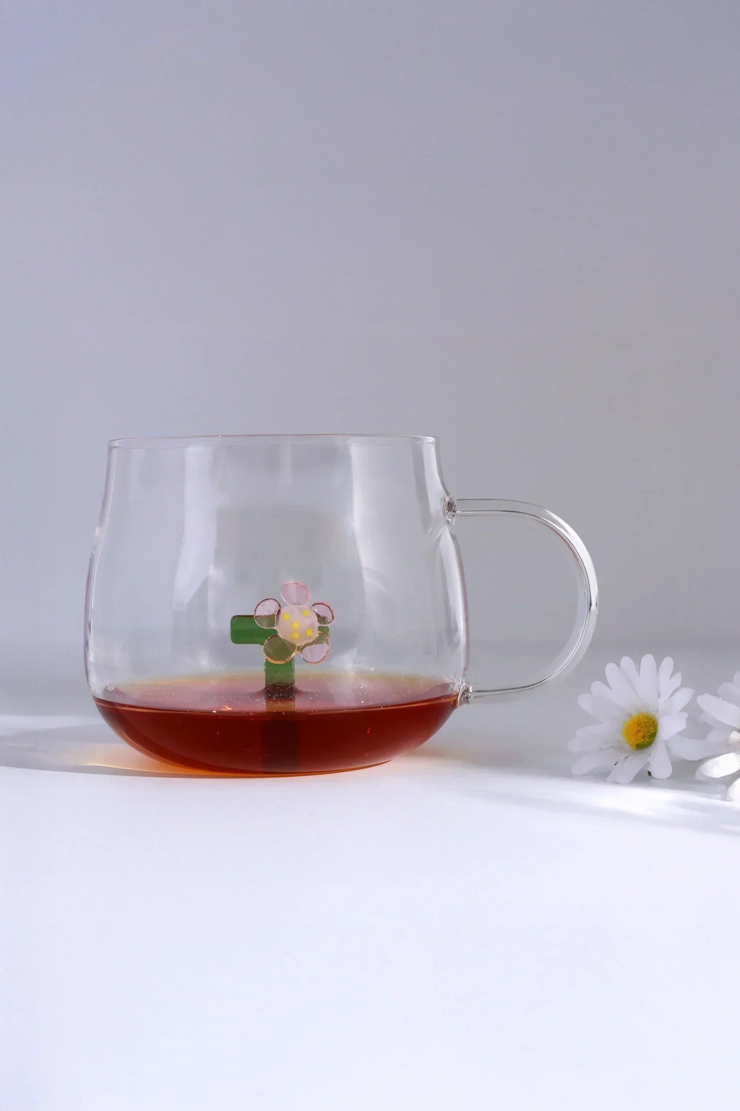 Clear glass mug with flower detail and tea, next to white daisies, G Decor luxury glassware.