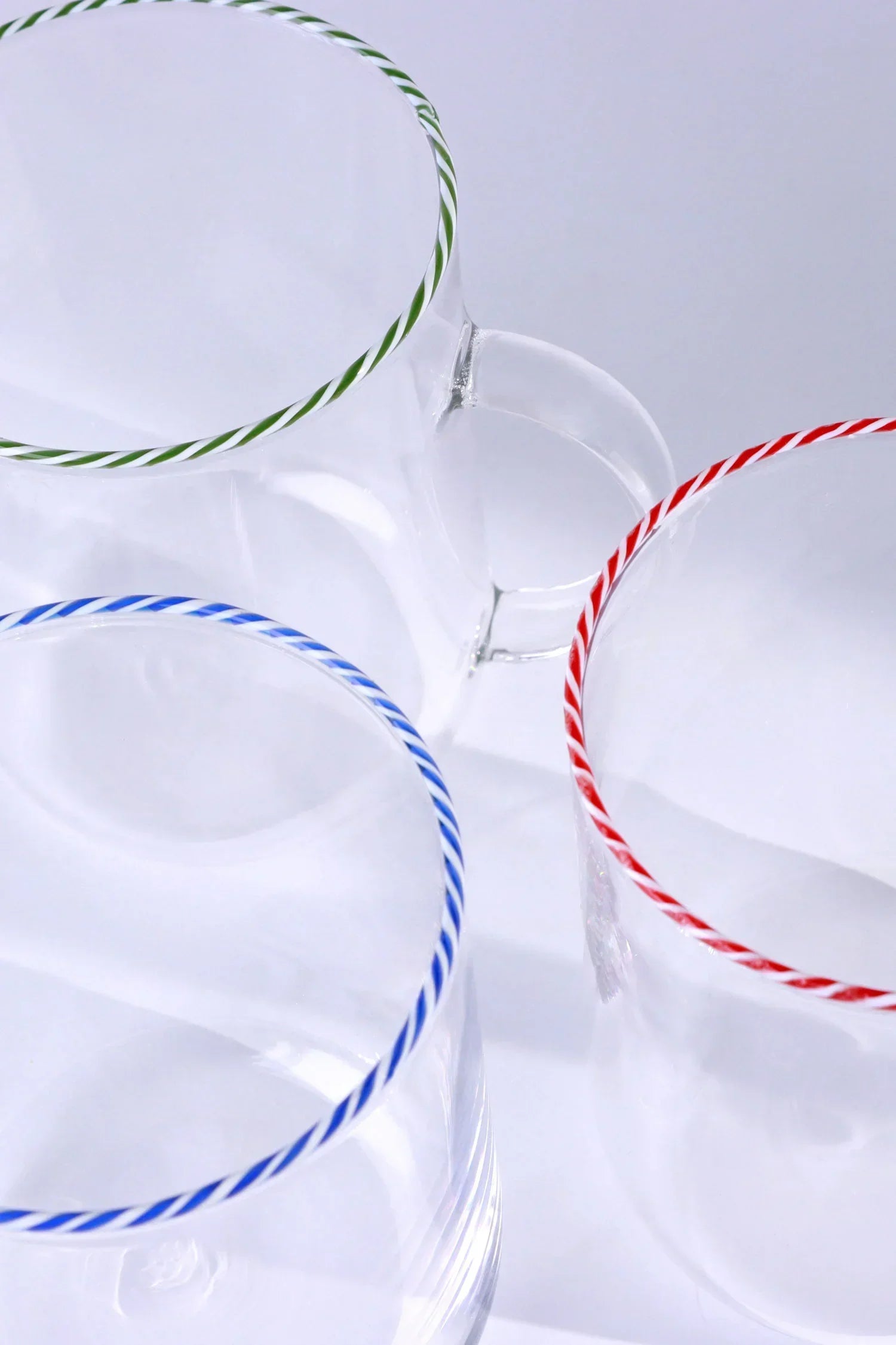 Set of clear G Decor glassware with green, red, and blue striped rims on white background