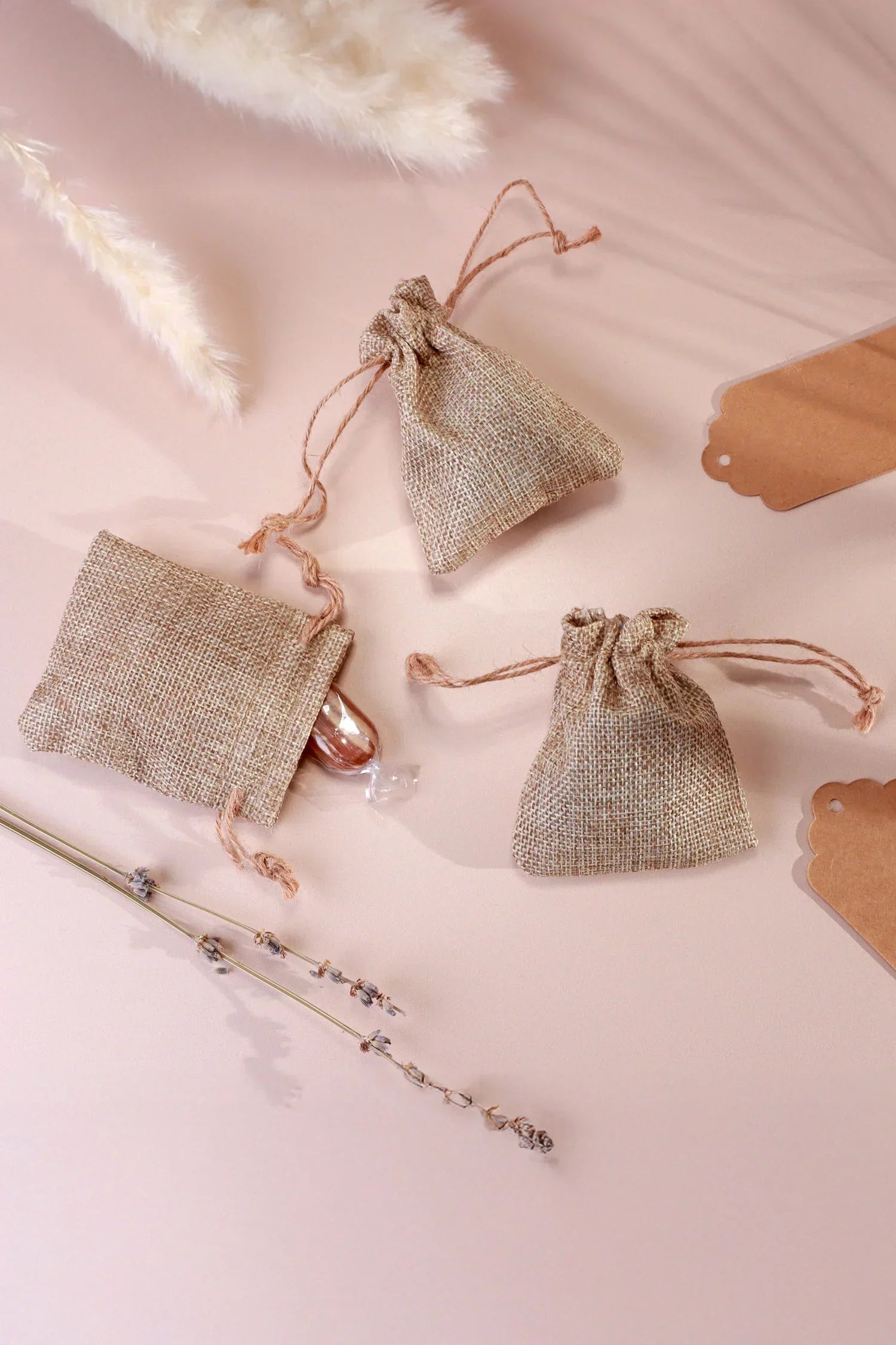 Natural jute gift pouches with tags and dried florals on soft pink surface, G Decor style