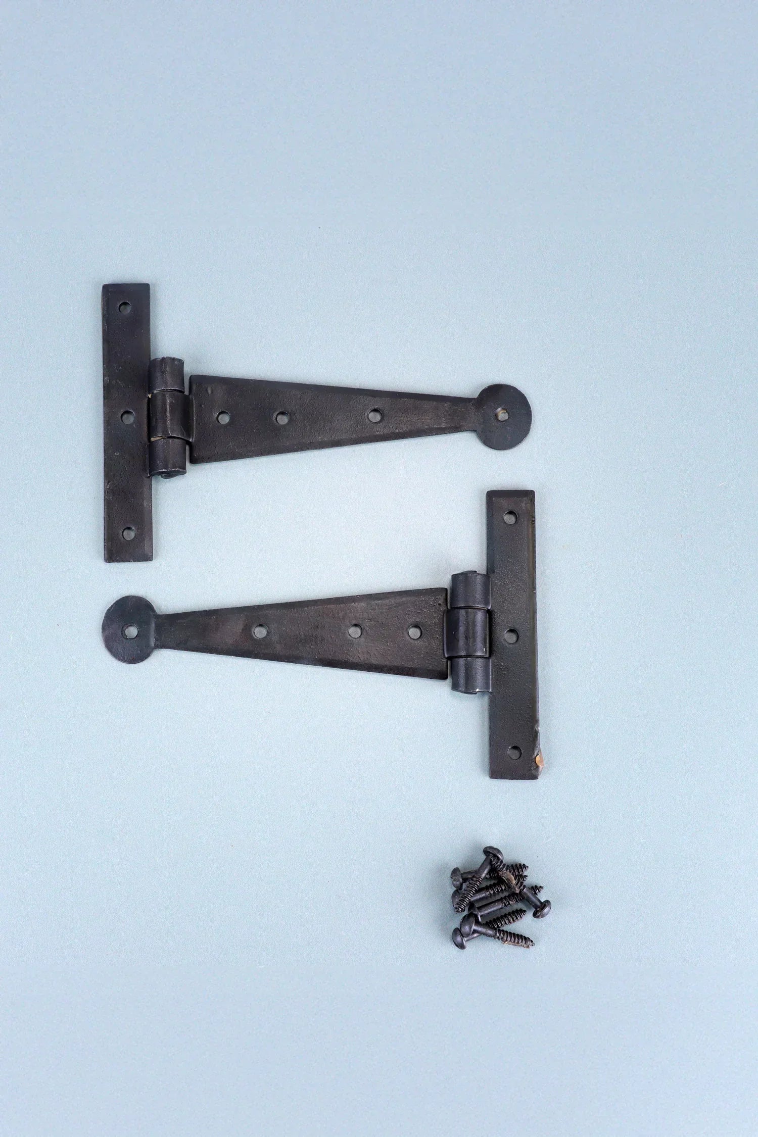 Black metal T-hinges with screws on a light blue background, G Decor luxury hardware