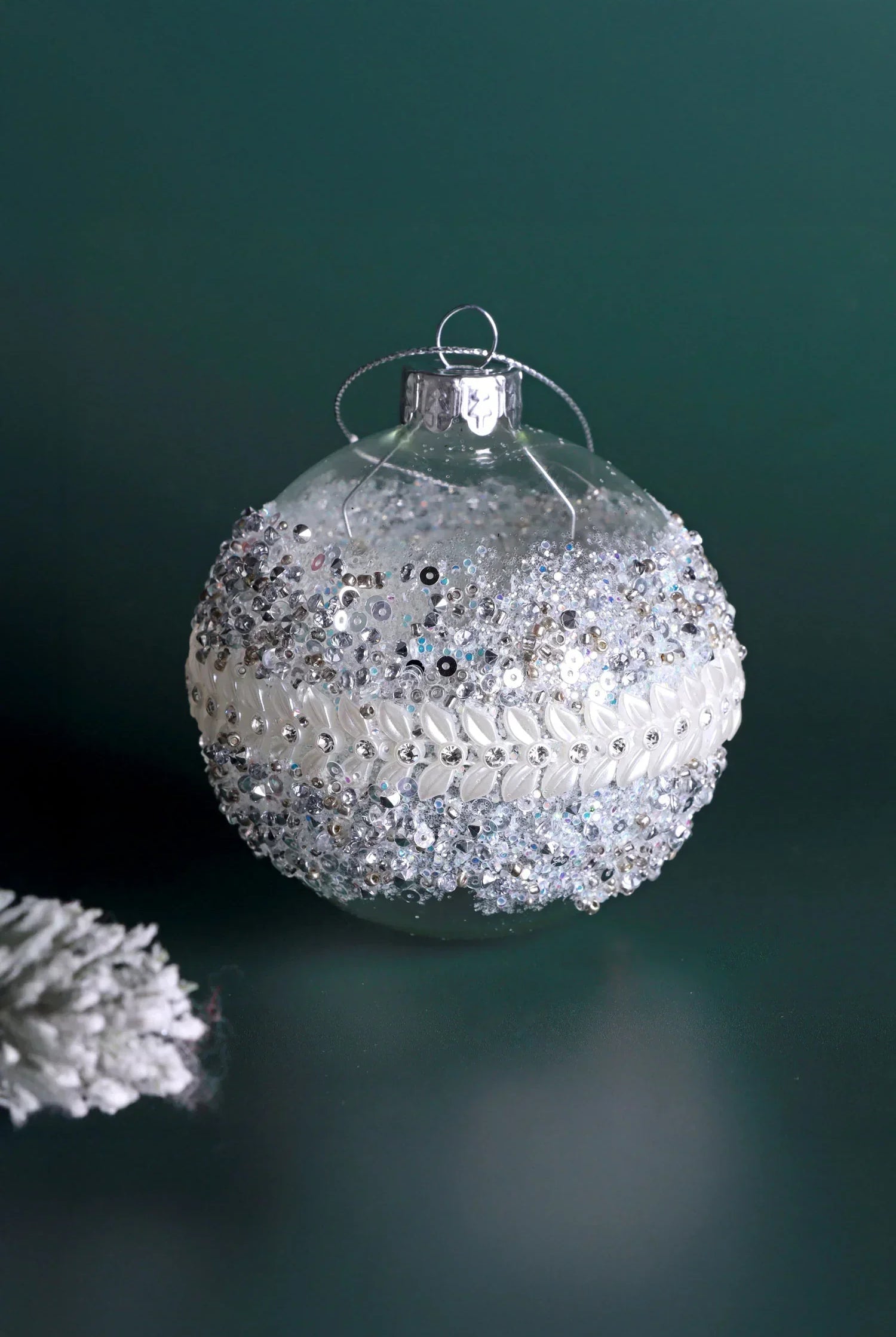 Luxury glass bauble with silver and white beads, G Decor home décor ornament on green background.