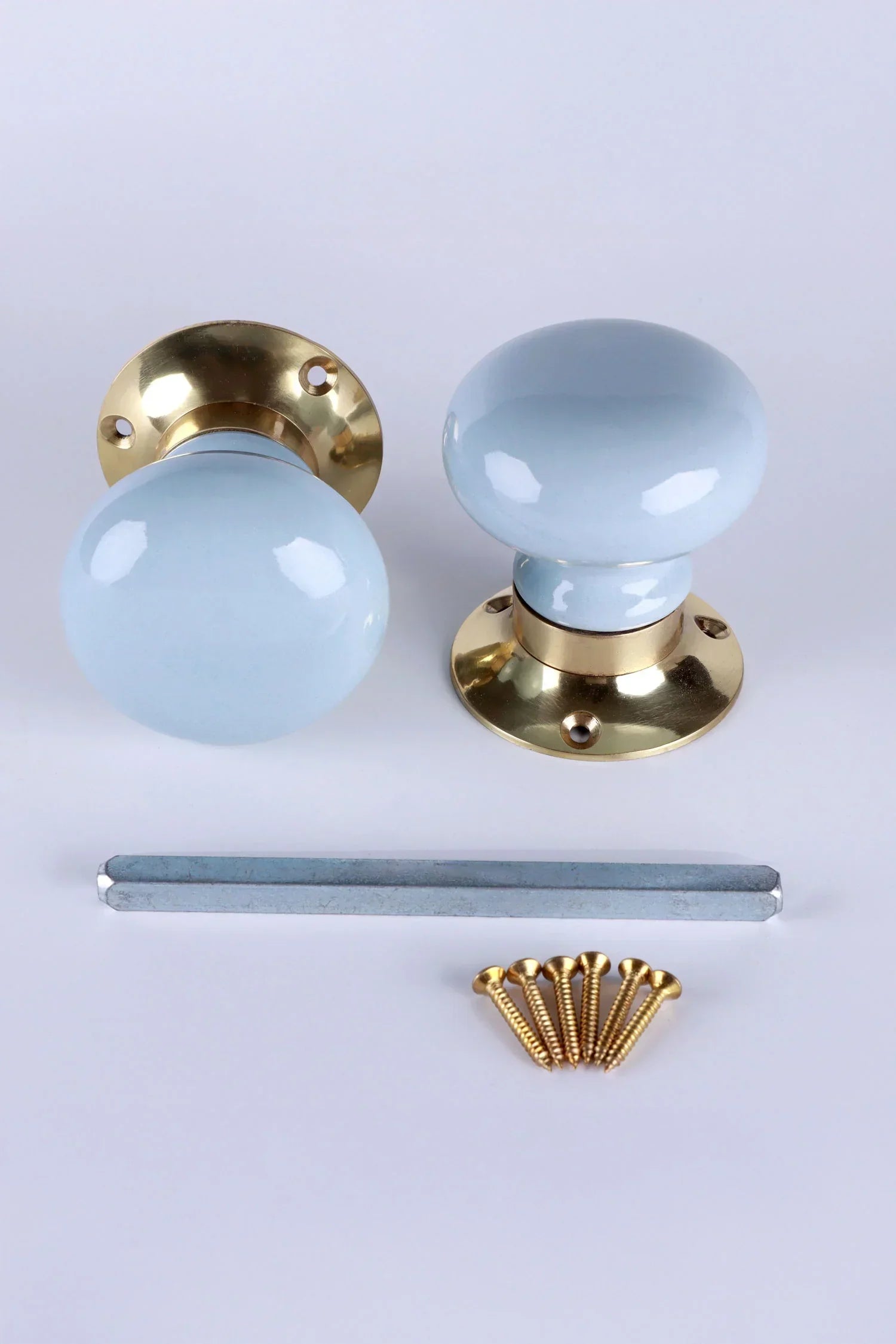 Pair of G Decor light blue and gold door knobs with installation screws and spindle on white background