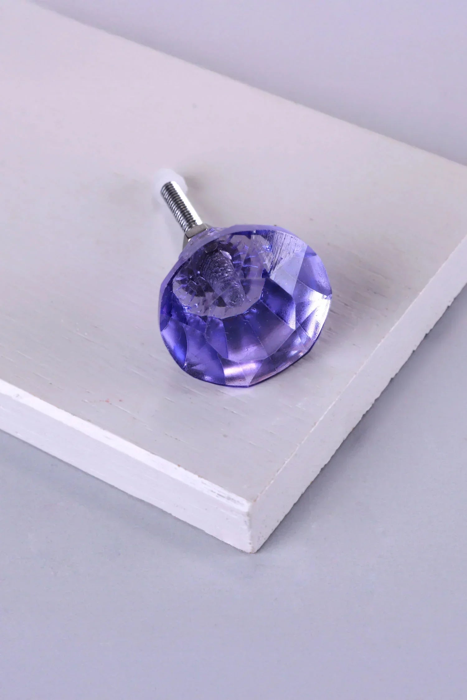 Faceted purple glass drawer knob with silver hardware on a white surface, luxury home decor