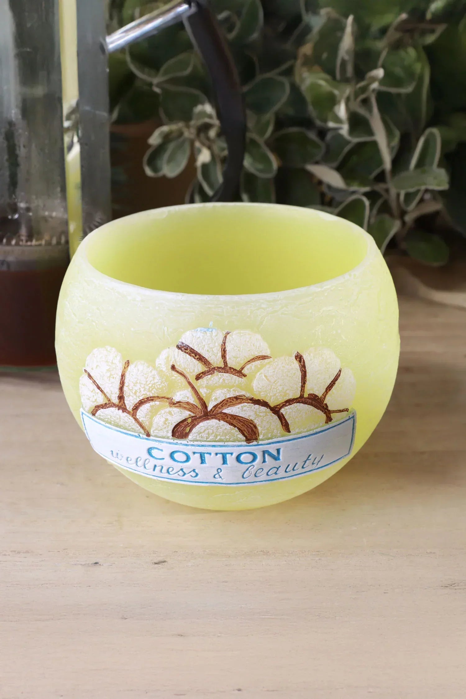 Yellow cotton wellness and beauty candle from G Decor on wooden surface with plant in background