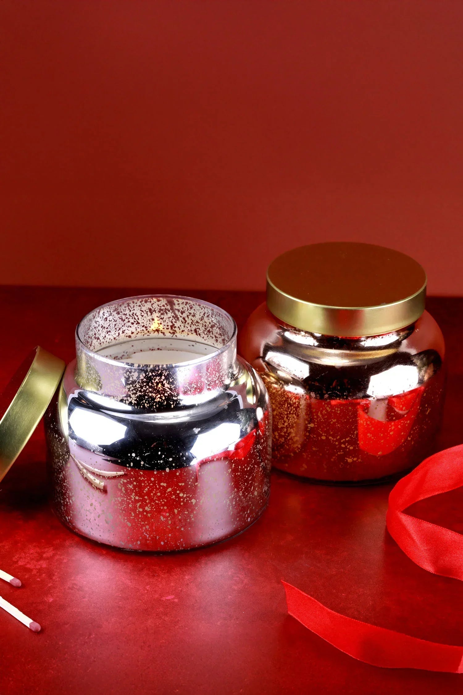 Luxury silver and gold glass candles with lids on a red surface, G Decor home décor