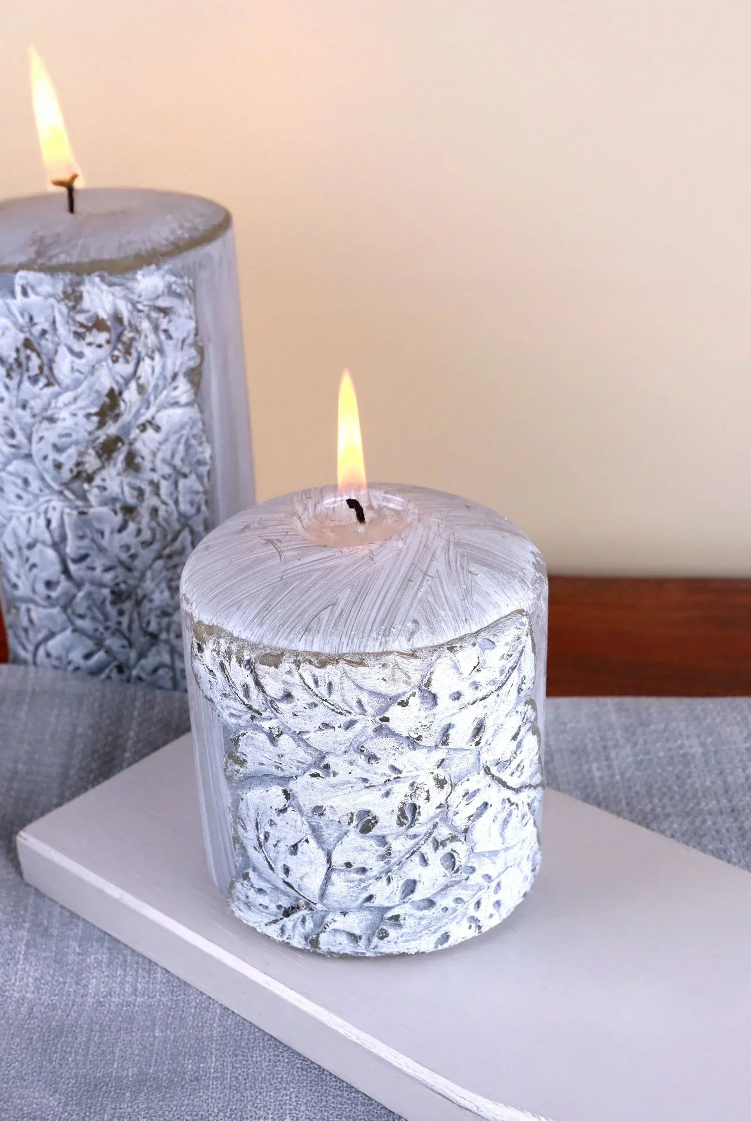 Decorative textured white pillar candle with leaf pattern lit on a grey table, G Decor home décor