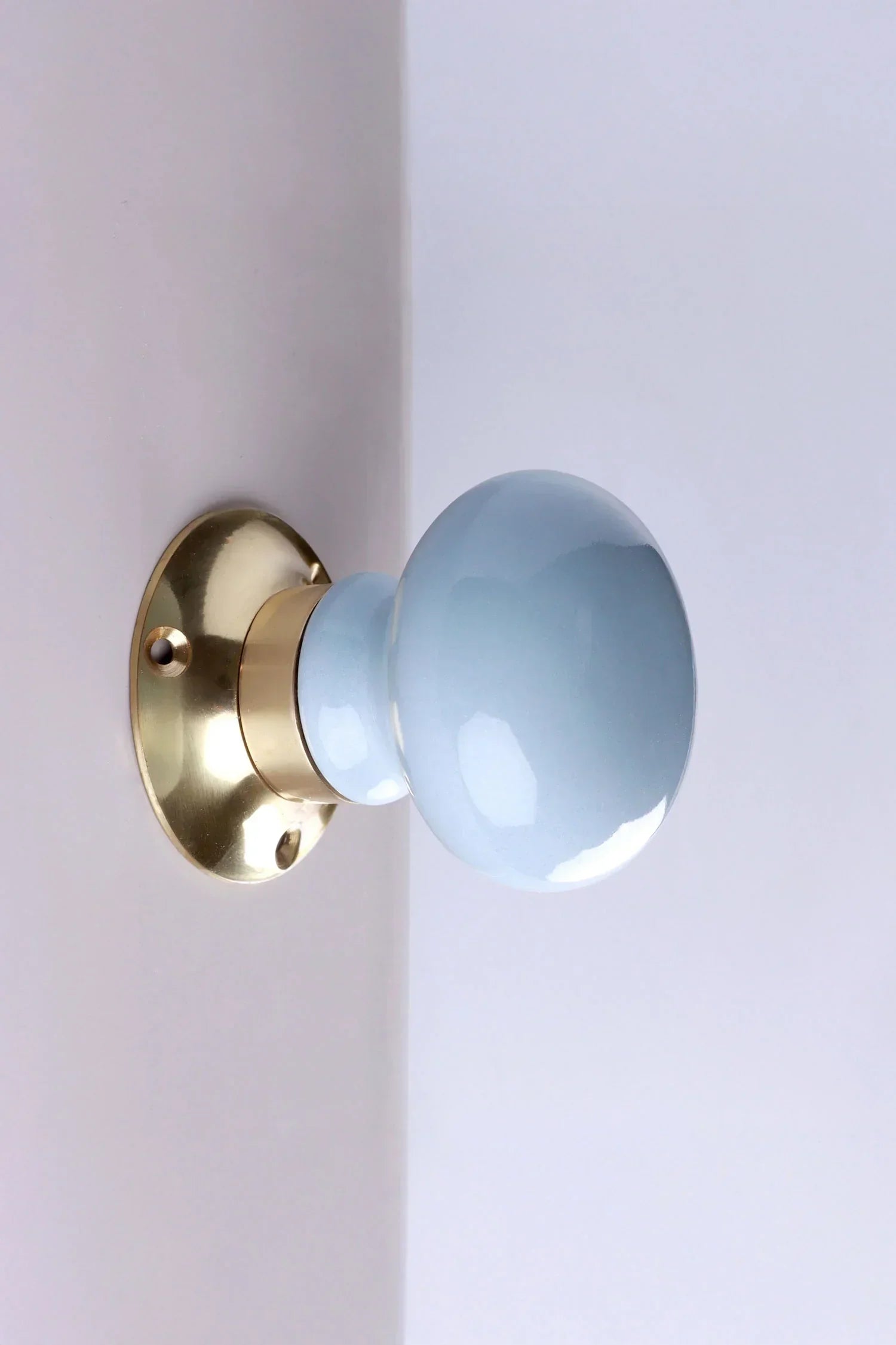 Light blue ceramic door knob with brass base on white wall, luxury hardware by G Decor