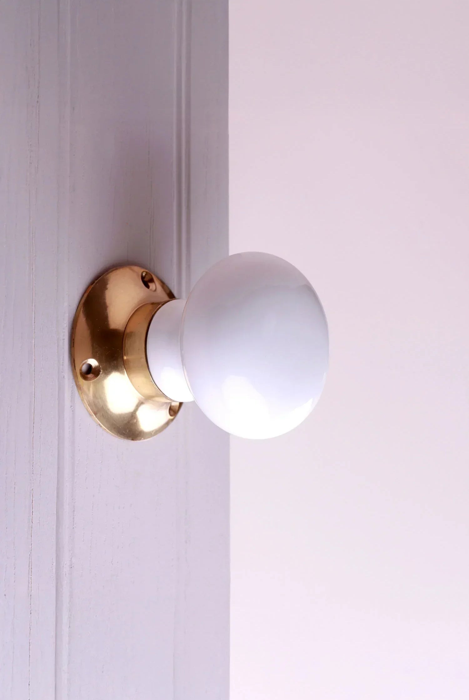 White ceramic door knob with gold base on a light wooden door, luxury home hardware by G Decor