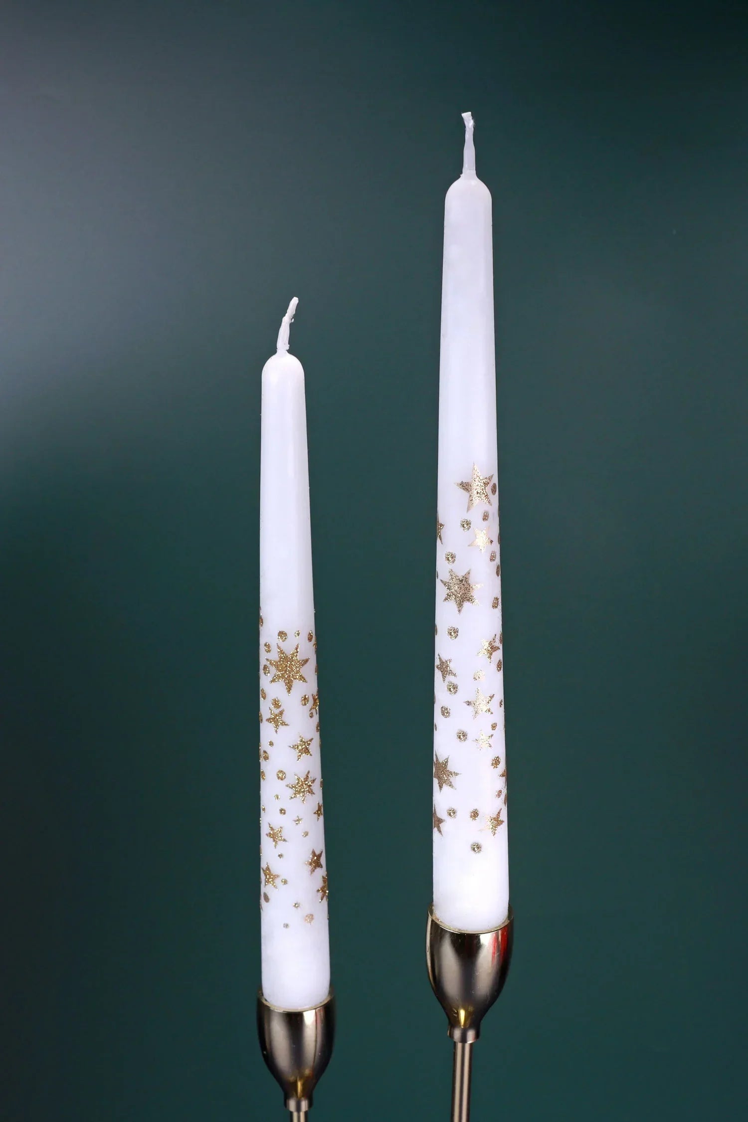 Two white taper candles with gold star patterns in metallic candle holders, home décor by G Decor.