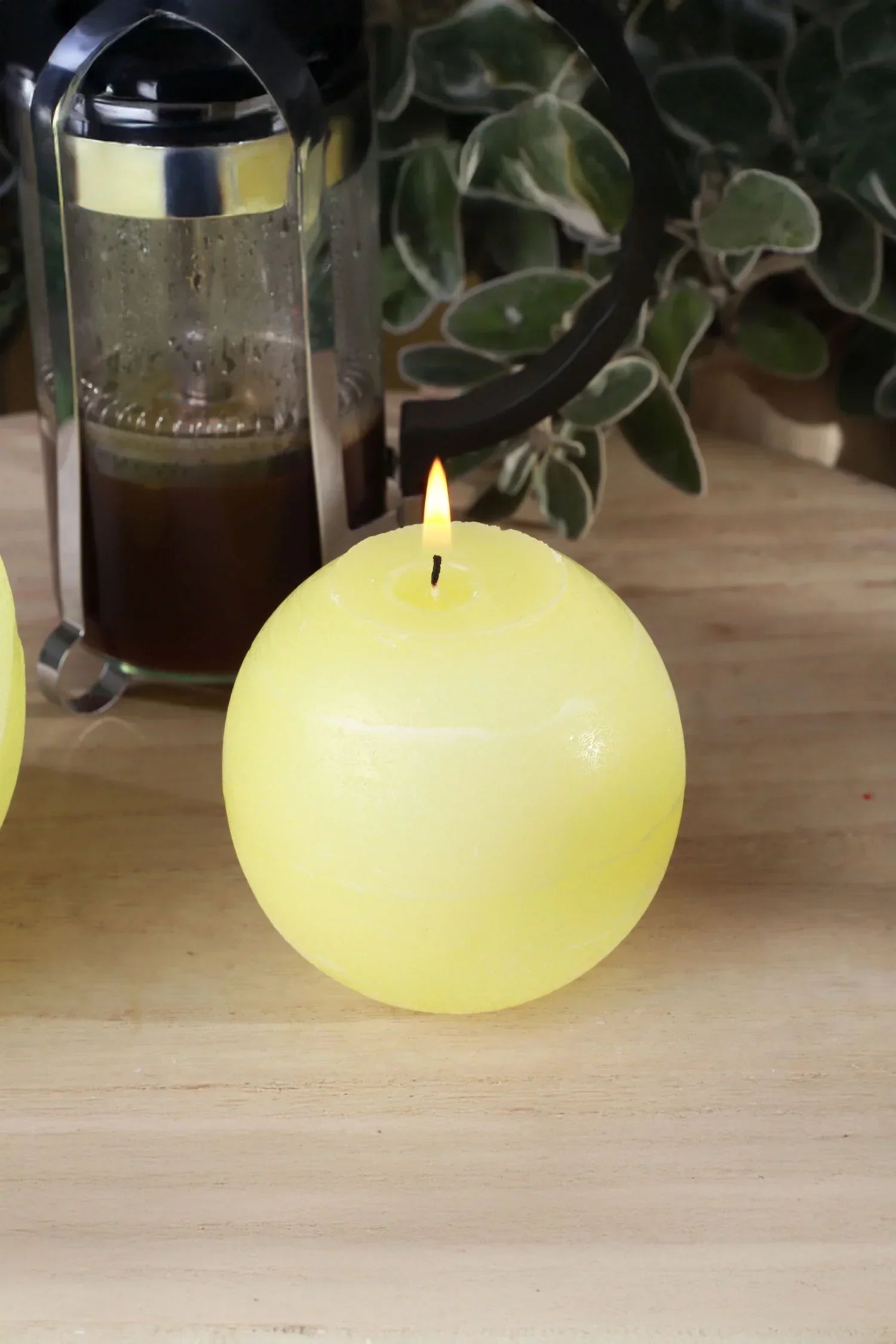 Yellow round candle lit on wooden table, French press and greenery behind, G Decor home décor