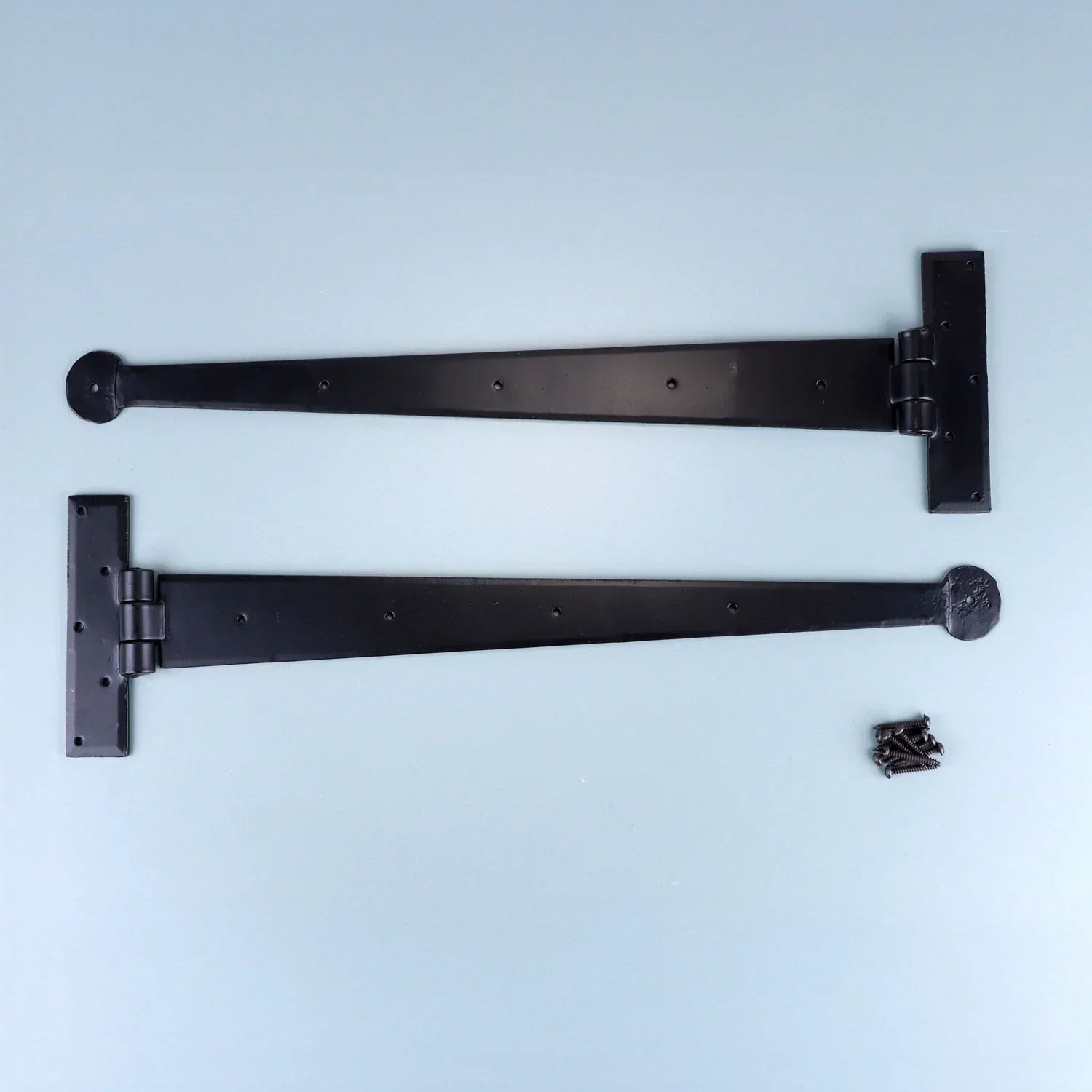 Pair of black metal T-hinges with screws, G Decor luxury hardware on light blue background.