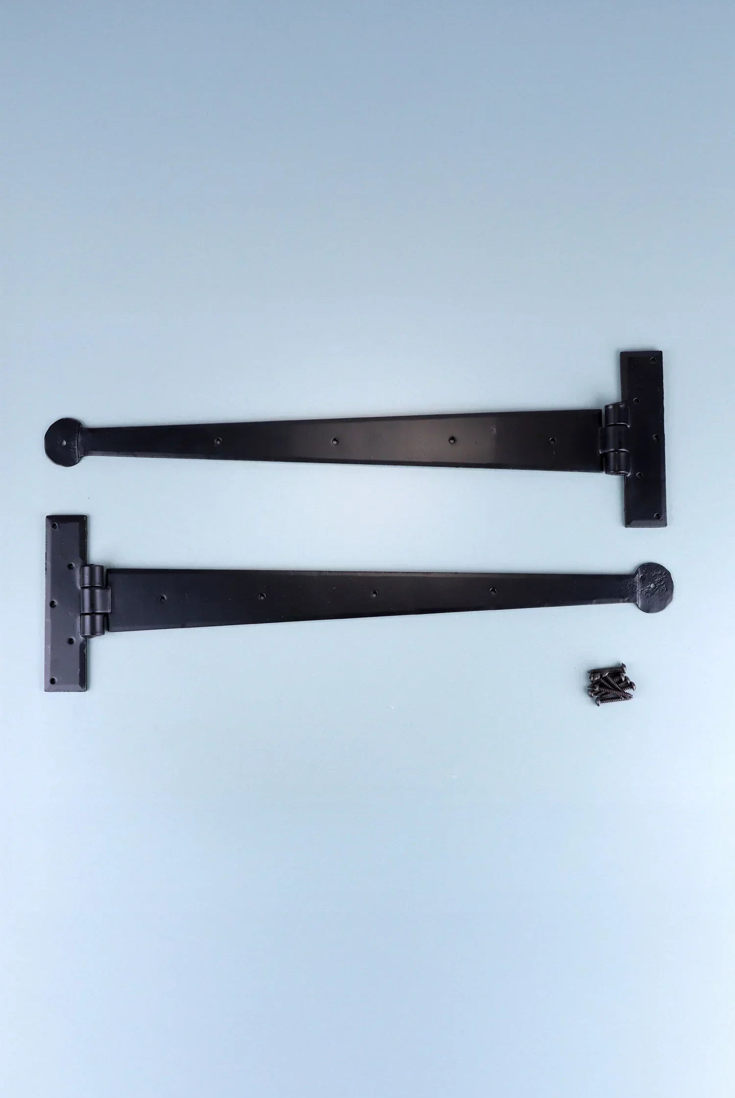 Pair of black metal T-hinges with screws, G Decor luxury hardware on light blue background.