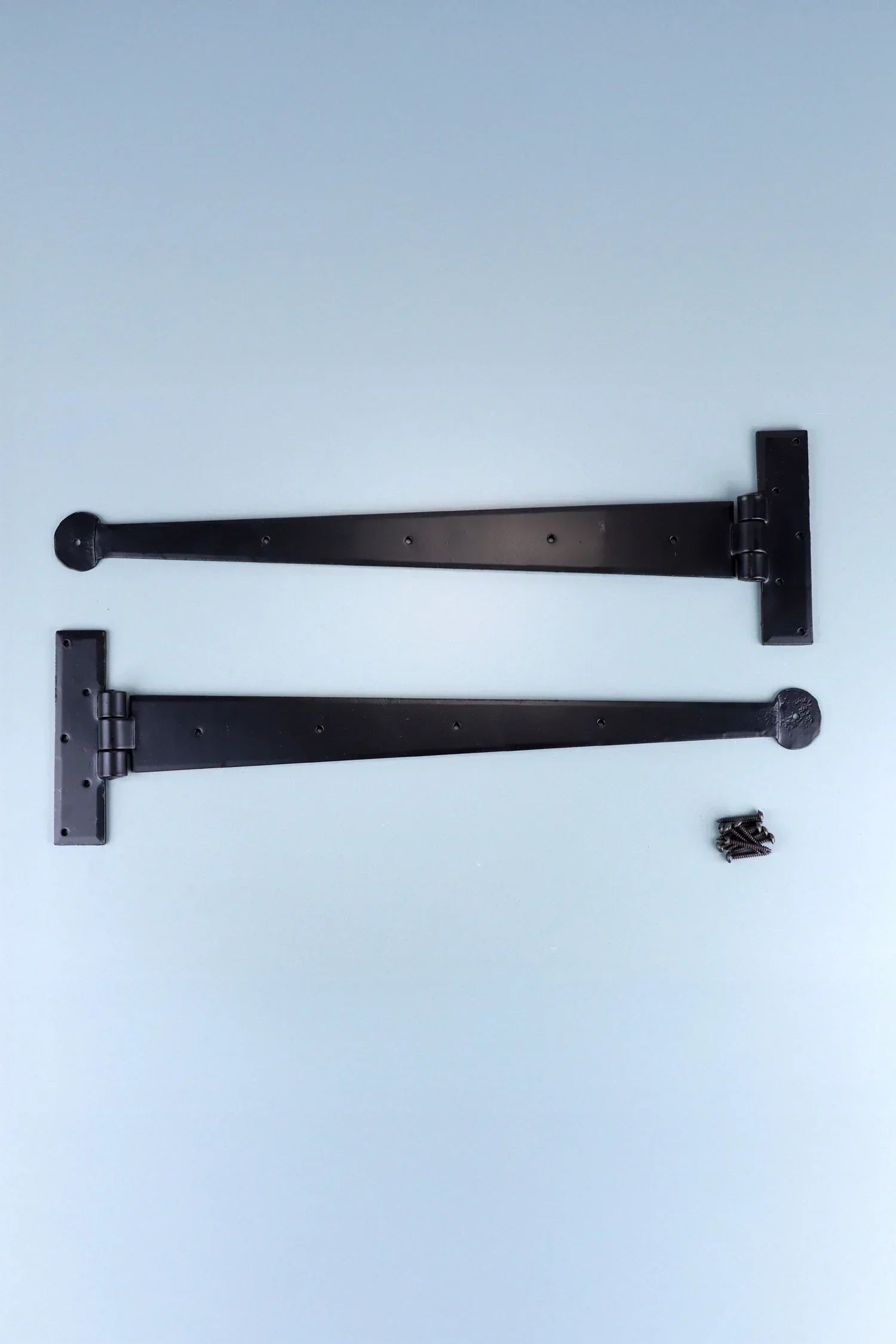 Pair of black metal T-hinges with screws, G Decor luxury hardware on light blue background.