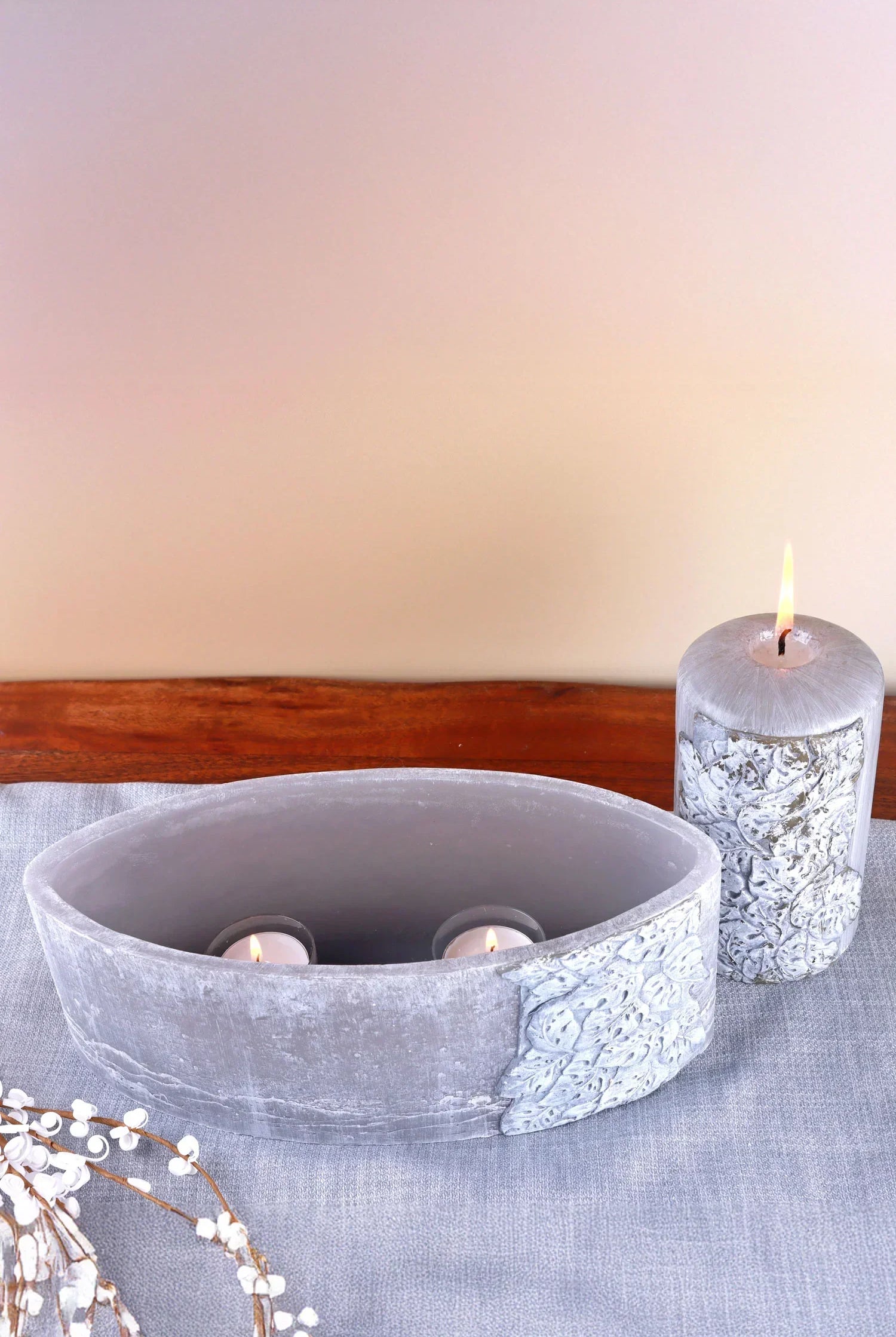 Decorative grey oval candle holder with two lit tealights and matching pillar candle on linen table for G Decor home décor.
