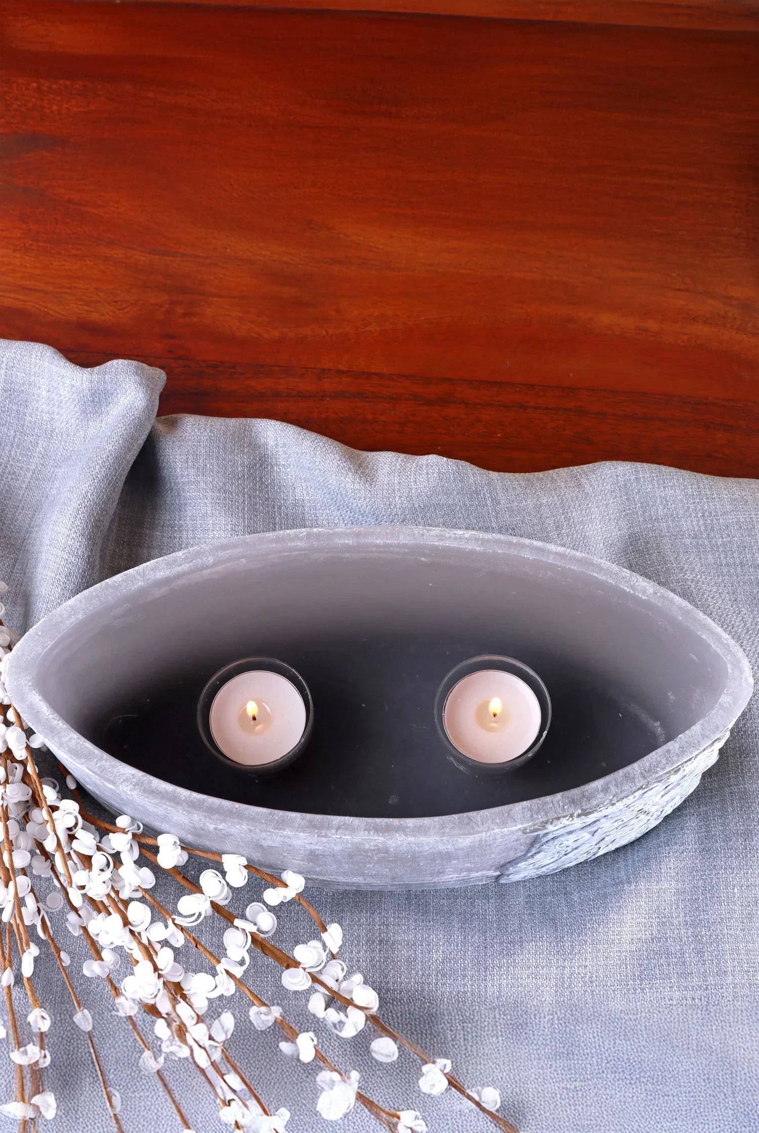 Decorative oval candle holder with two tealight candles and faux white florals on a grey cloth
