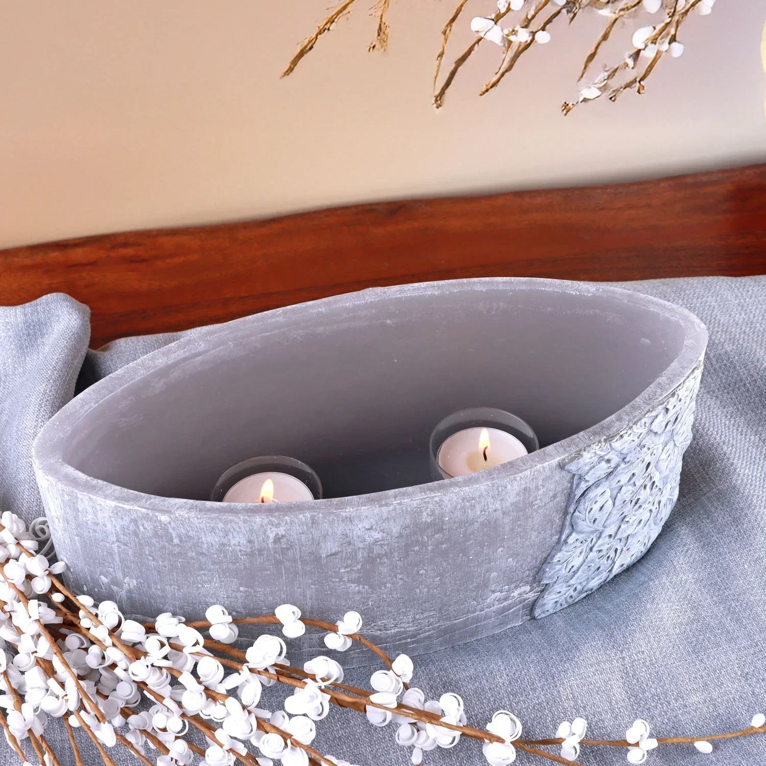 Oval grey decorative vase with tealight candles and white faux floral branches on wooden table