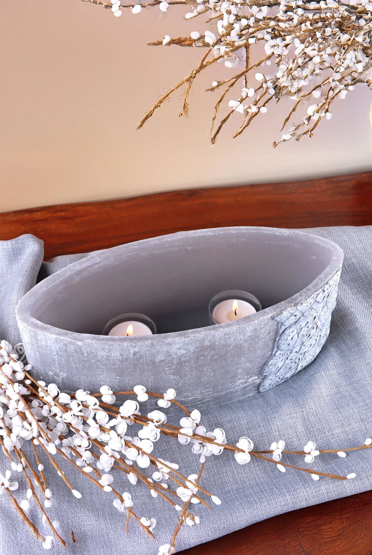 Oval grey decorative vase with tealight candles and white faux floral branches on wooden table