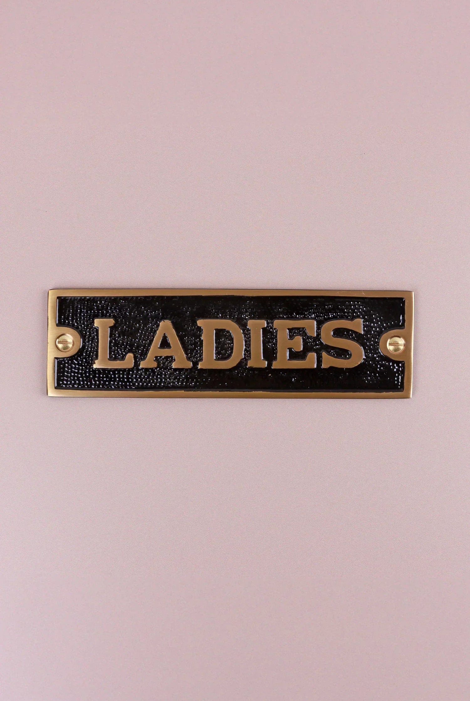 Gold and black metal 'Ladies' door sign on a light pink wall, G Decor home hardware